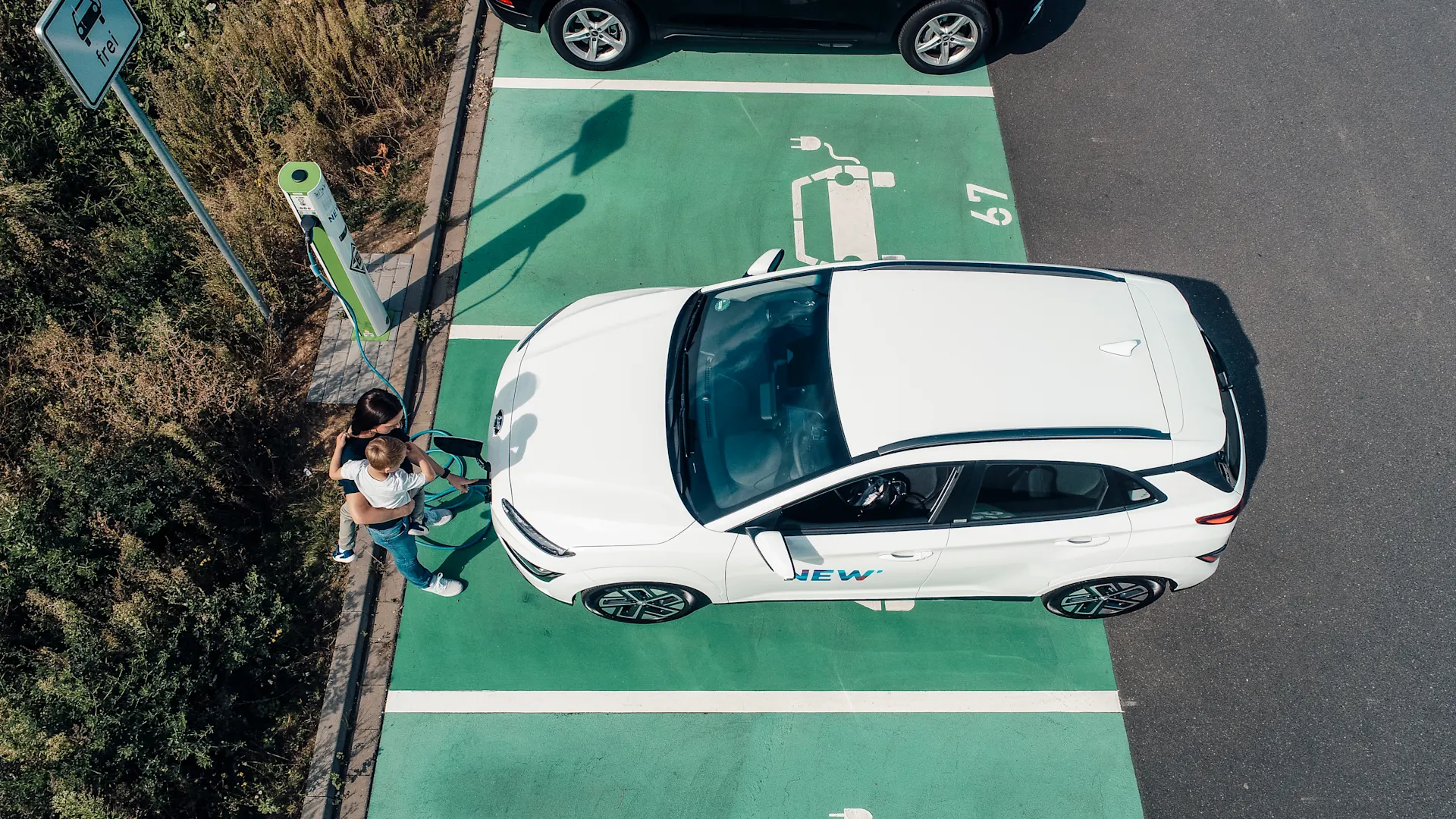 Entspanntes E-Laden Kind sitzt während das Auto an einer Ladestation der NEW Energie lädt bei der Mutter auf dem Arm.