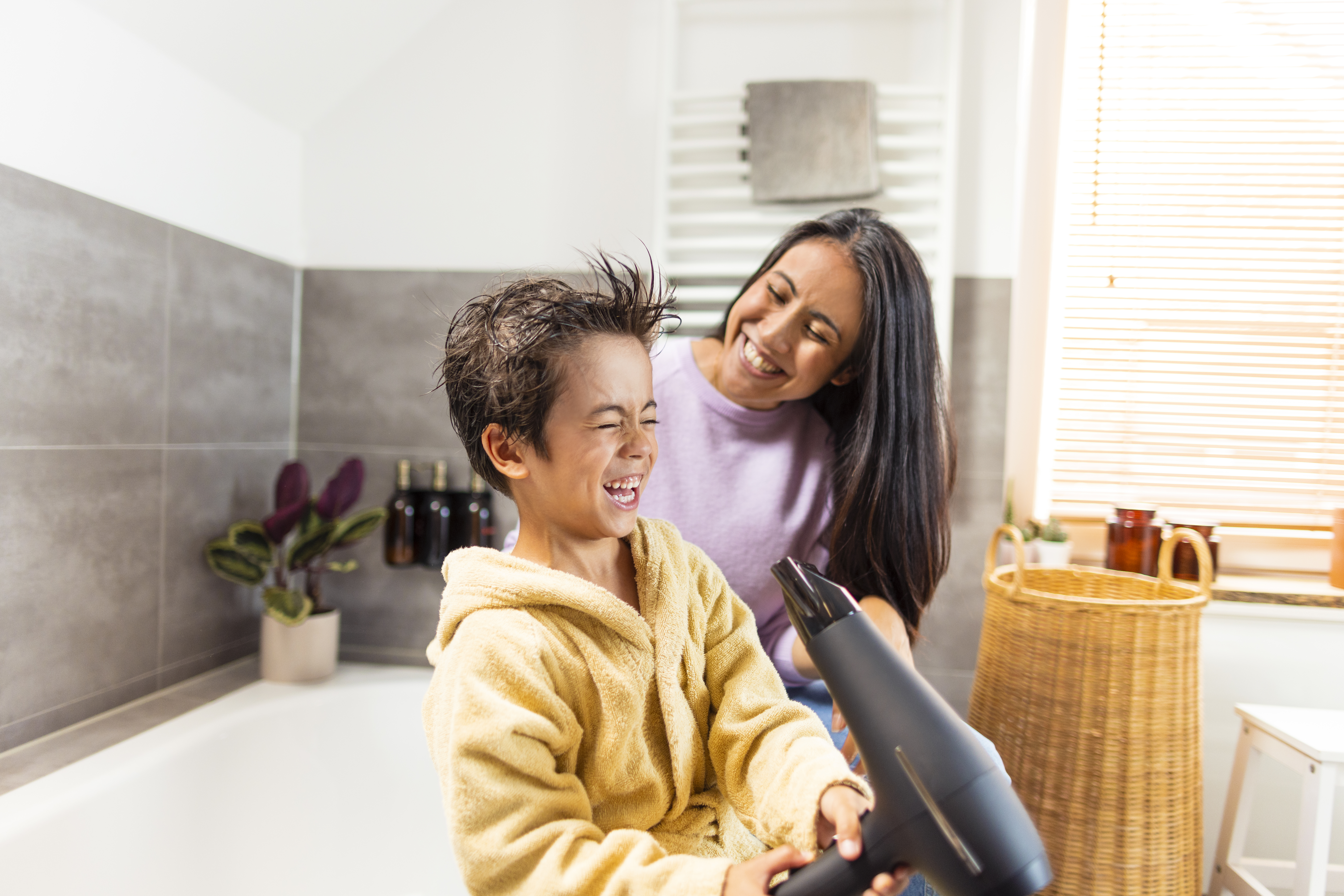 Ein kleiner Junge föhnt sich im Beisein seiner Mutter die Haare im Badezimmer. Strom bekommt der Föhn durch die NEW Energie. 