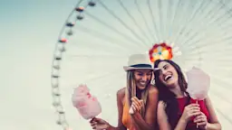 Freundinnen vor Riesenrad Zwei Freundinnen stehen vor einem Riesenrad und essen Zuckerwatte gemeinsam. Sie freuen sich über die Vorteile bei der NEW Energie.