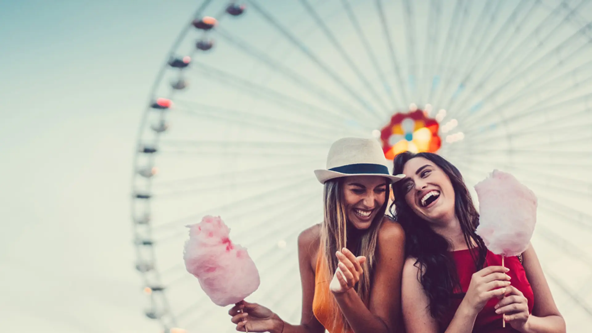 Zwei Freundinnen stehen vor einem Riesenrad und essen Zuckerwatte gemeinsam. Sie freuen sich über die Vorteile bei der NEW Energie.