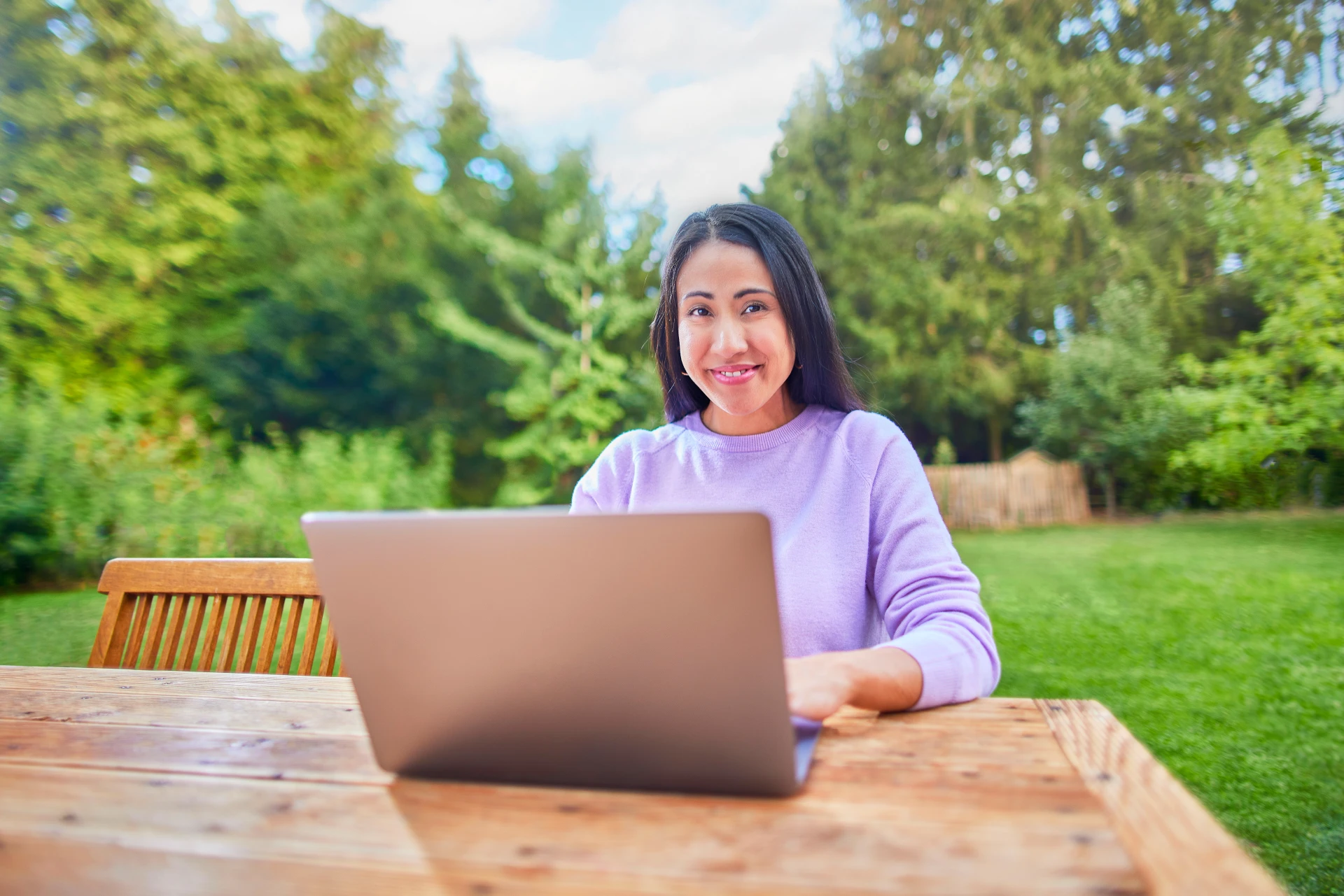 Eine Frau sitzt mit ihrem Laptop im Garten und informiert sich über die Tarifauswahl.