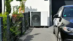 Wärmepumpe an der Garage Eine Wärmepumpe steht an einer Garage im Außenbereich.