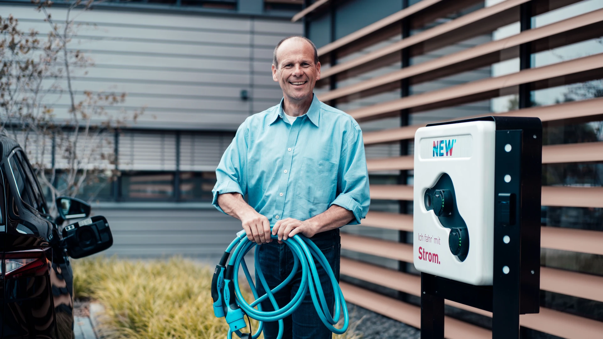 Ein Mann steht mit einem Ladekabel vor einer Ladesäule der NEW Energie.