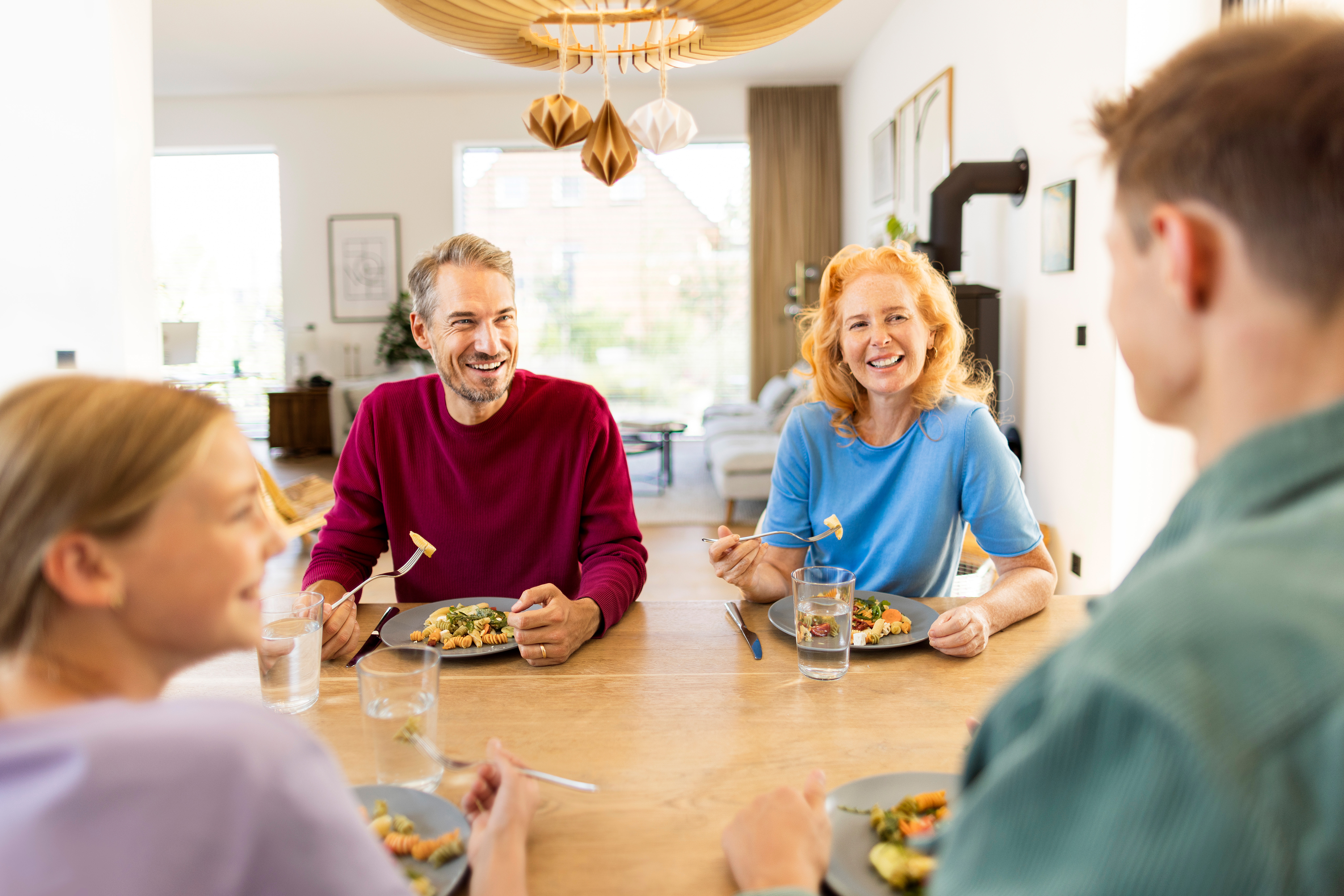 Eine Familie sitzt an einem Esstisch zum Familienessen und unterhält sich über die Stromtarife des Stromanbieters NEW Energie.
