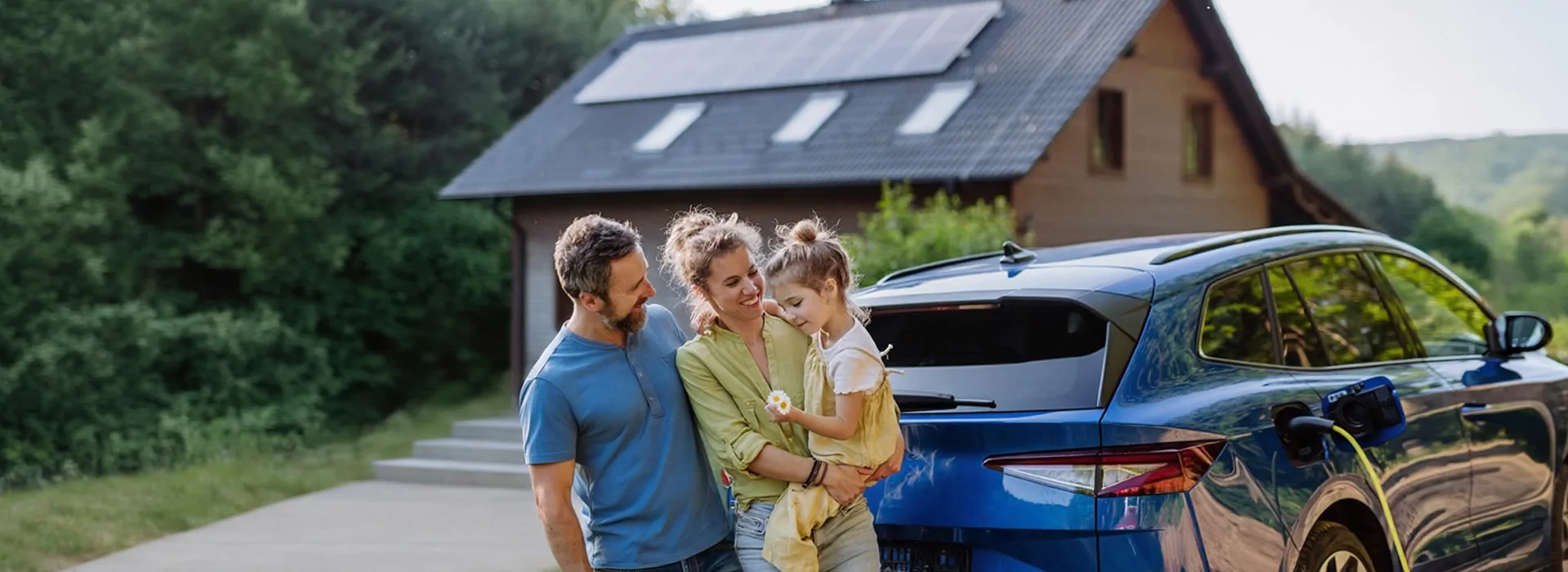 Familie vor Haus mit PV-Anlage und Elektroauto Eine Familie steht an einem Elektroauto was gerade geladen wird. Im Hintergrund ist ein Haus mit einer Photovoltaik-Anlage auf dem Dach zu sehen.