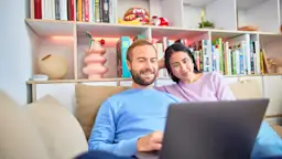 Familie an Laptop Ein Paar sitzt auf dem Sofa und vergleicht am Laptop Tarife der NEW Energie.