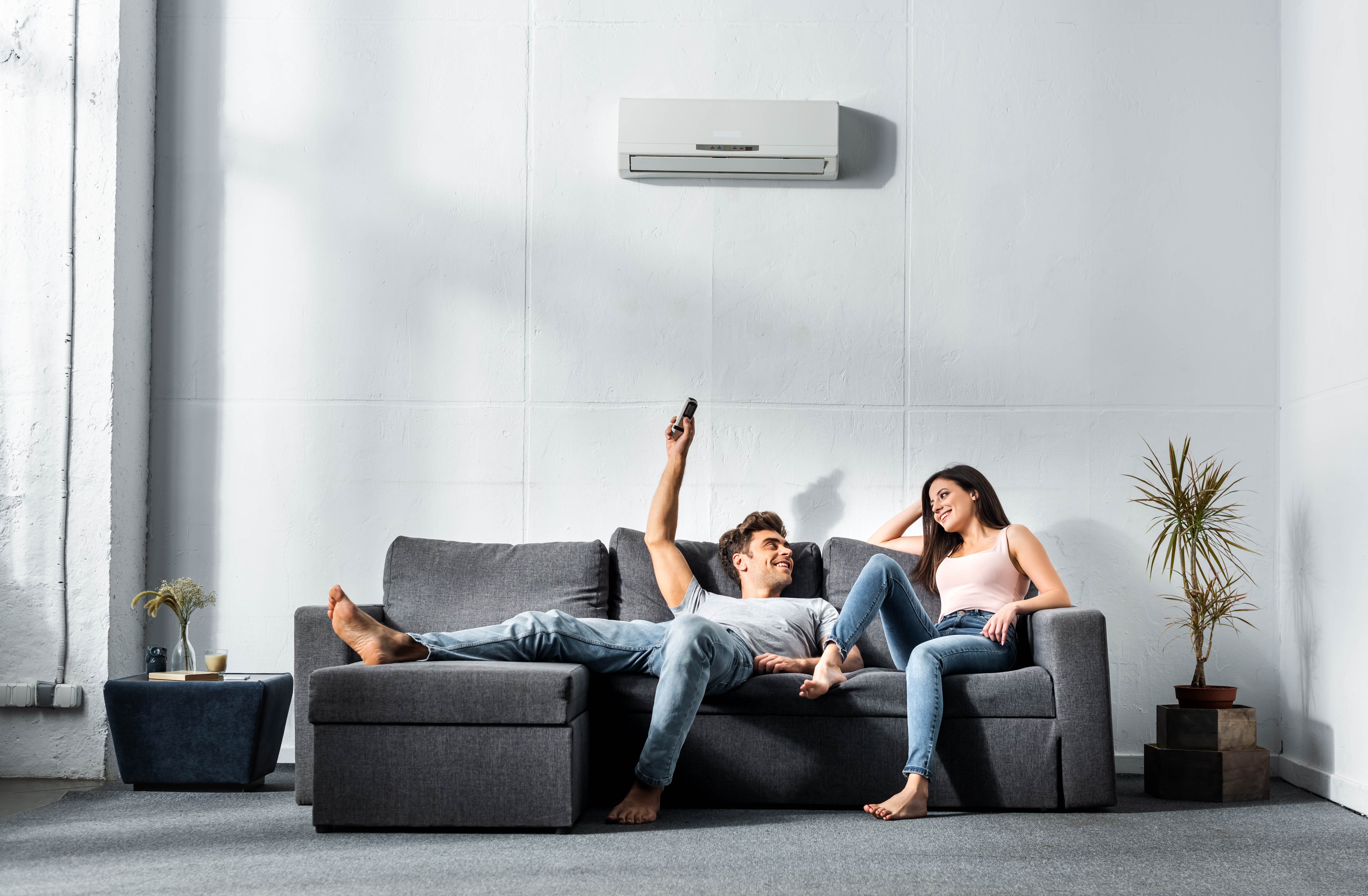 Zwei Personen sitzen im Wohnzimmer auf einem dunklem Sofa und nutzen energieeffiziente Technik – mit Strom von NEW Energie.