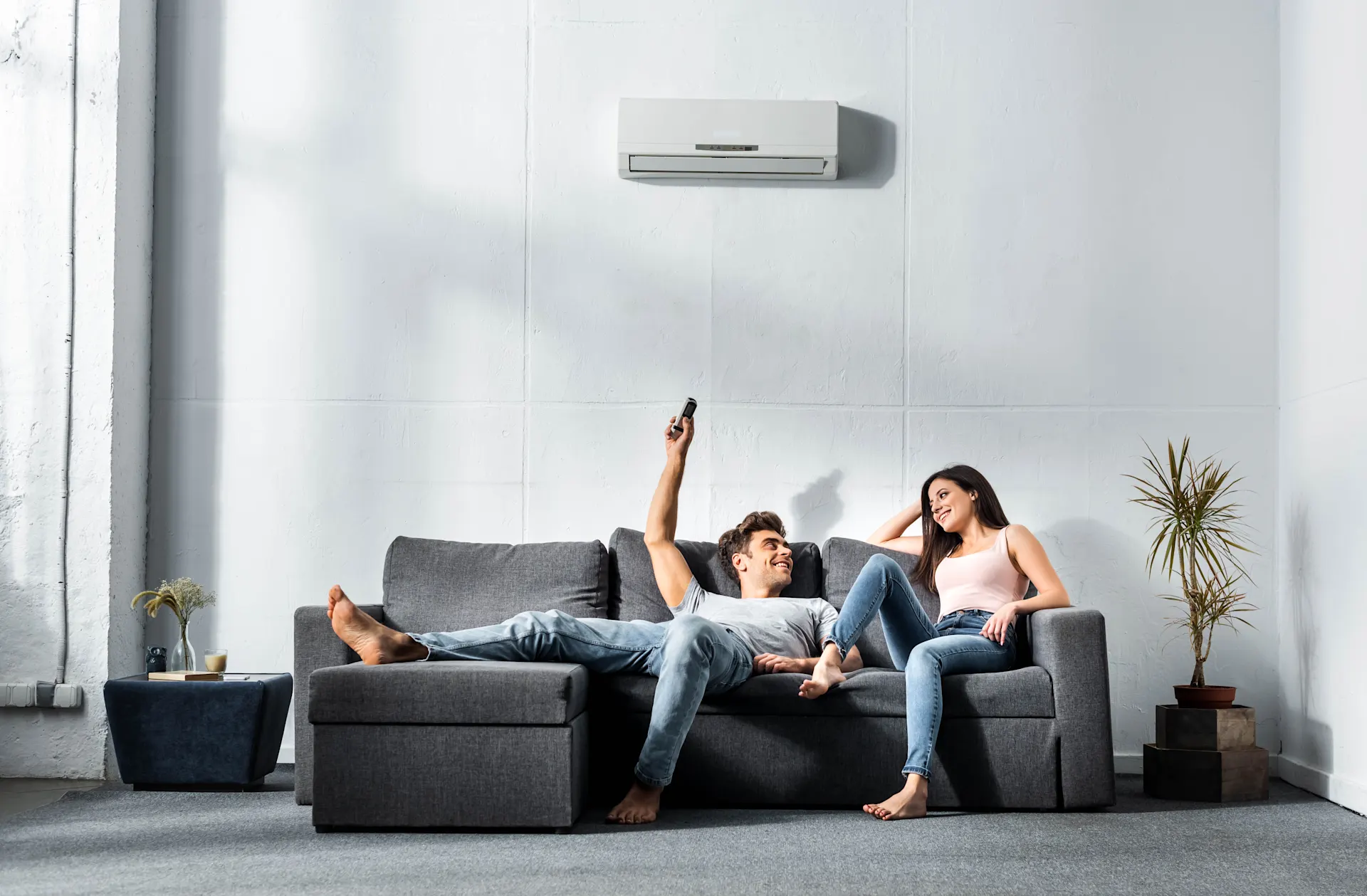 Zwei Personen sitzen im Wohnzimmer auf einem dunklem Sofa und nutzen energieeffiziente Technik – mit Strom von NEW Energie.