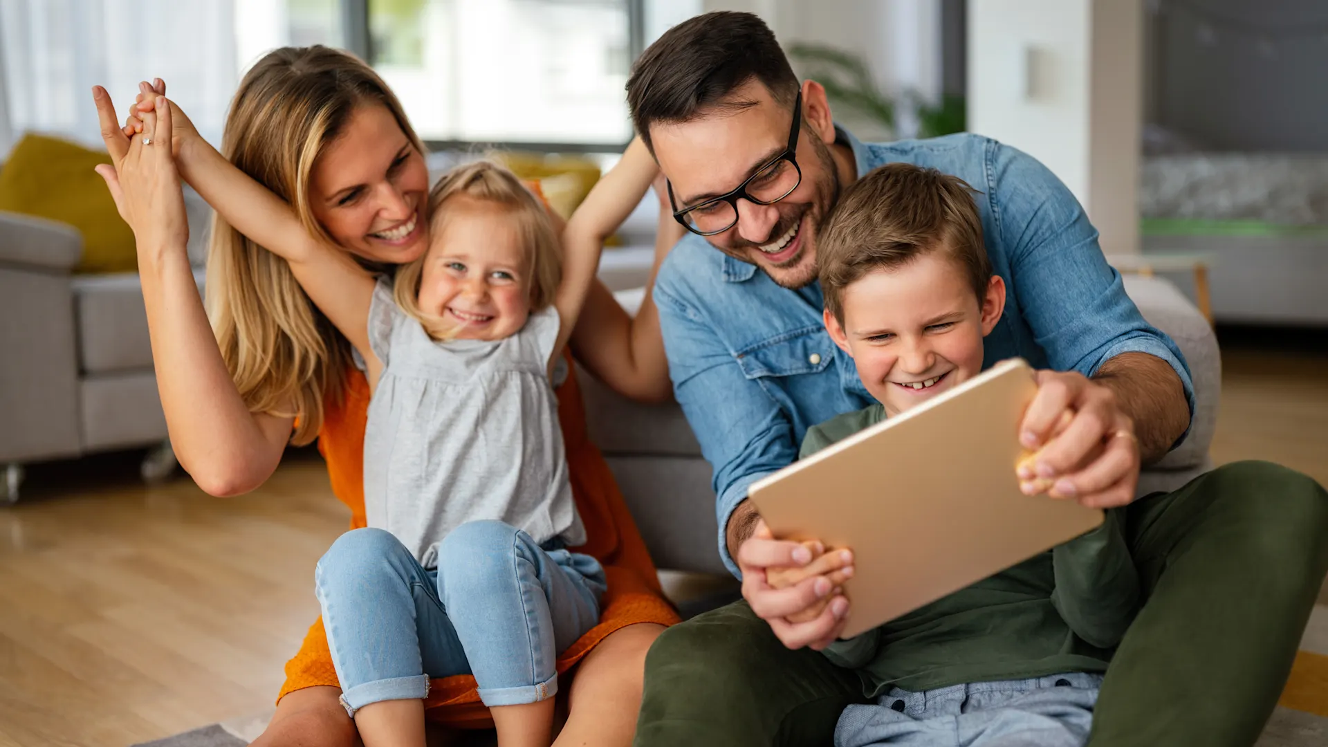 Familienzeit im Wohnzimmer Die Eltern spielen zusammen mit ihren Kindern auf dem Boden. Sie freuen sich über günstige Tarife der NEW Energie.