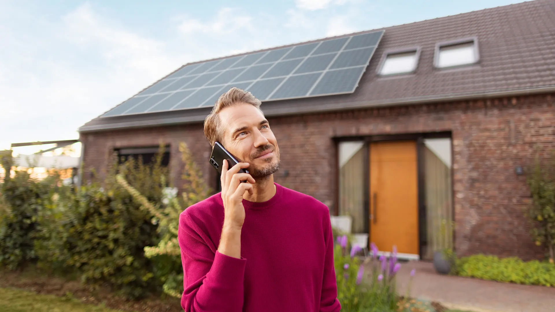 Telefonat über Photovoltaikanlagen Ein Mann telefoniert im Garten vor seinem Haus, mit einer Photovoltaik Anlage von der NEW Energie auf dem Dach.