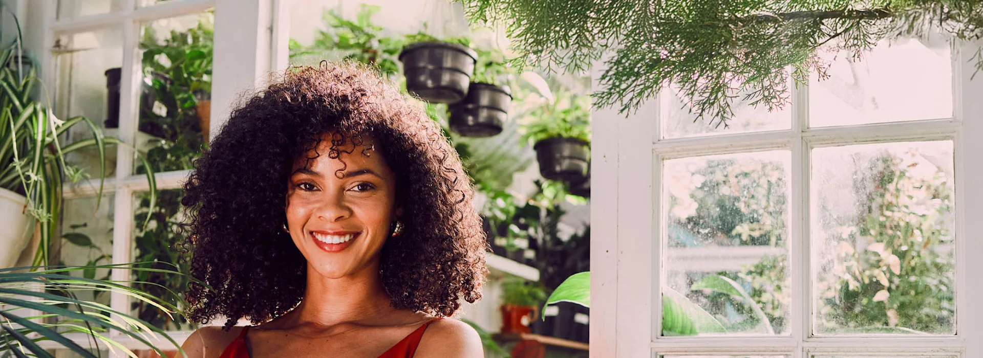 Frau im grünen mit einigen Pflanzen Eine Frau steht zwischen vielen grünen Pflanzen in ihrem Wohnzimmer.