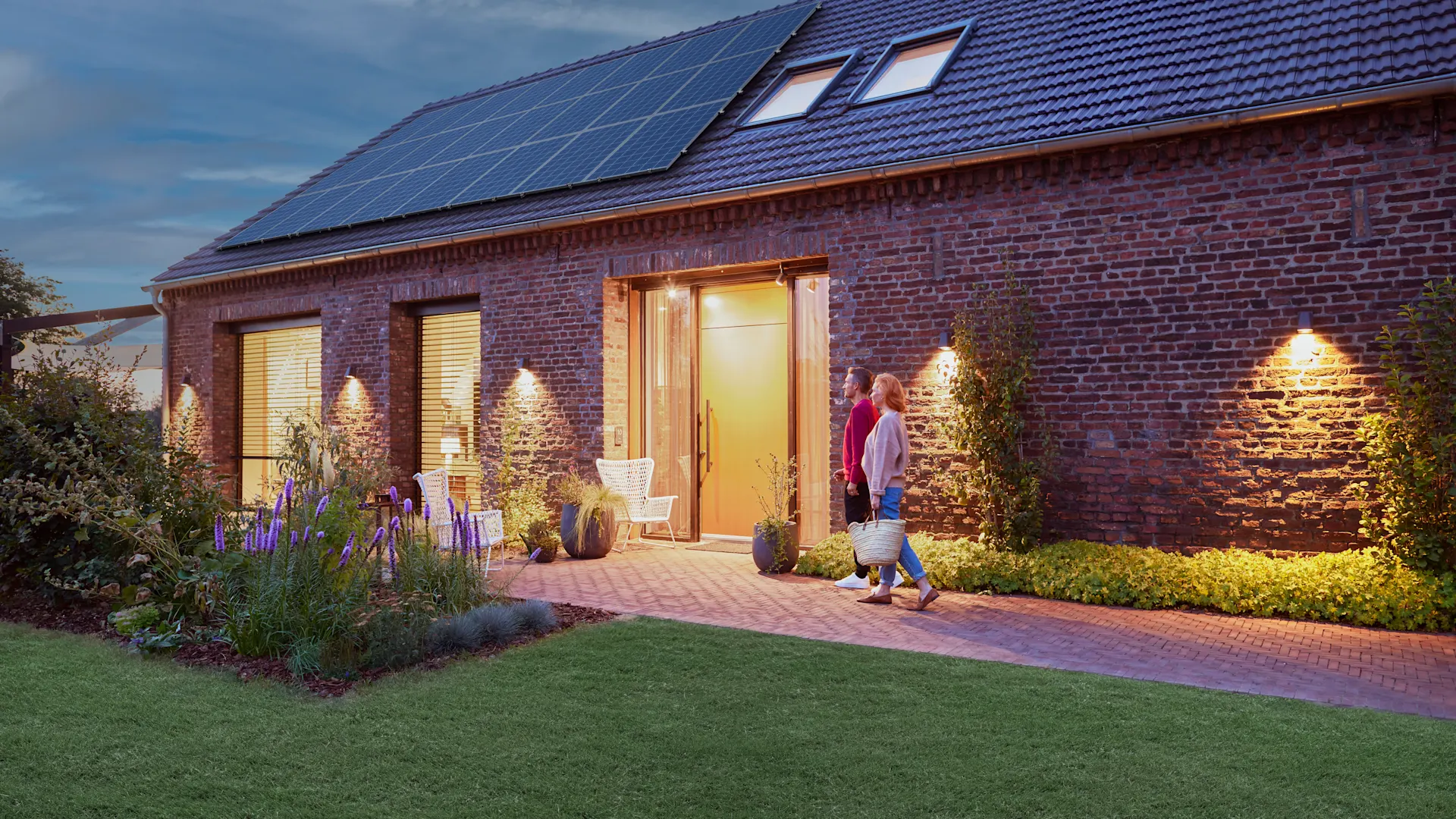 Günstige Stromtarife für die Wohnungswirtschaft Ein Paar geht am Abend vor ihrem Haus her, welches mit einem Energiedach der NEW-Energie ausgestattet ist.