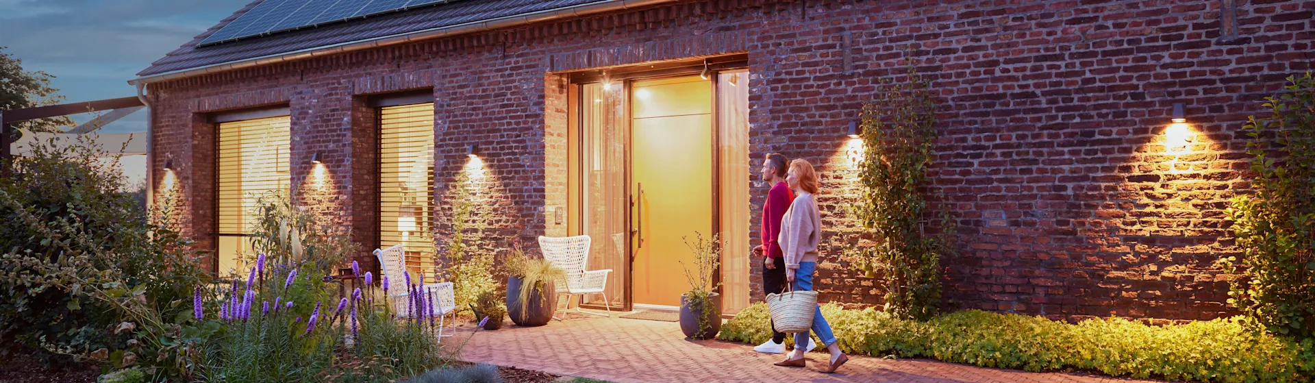 Günstige Stromtarife für die Wohnungswirtschaft Ein Paar geht am Abend vor ihrem Haus her, welches mit einem Energiedach der NEW-Energie ausgestattet ist.