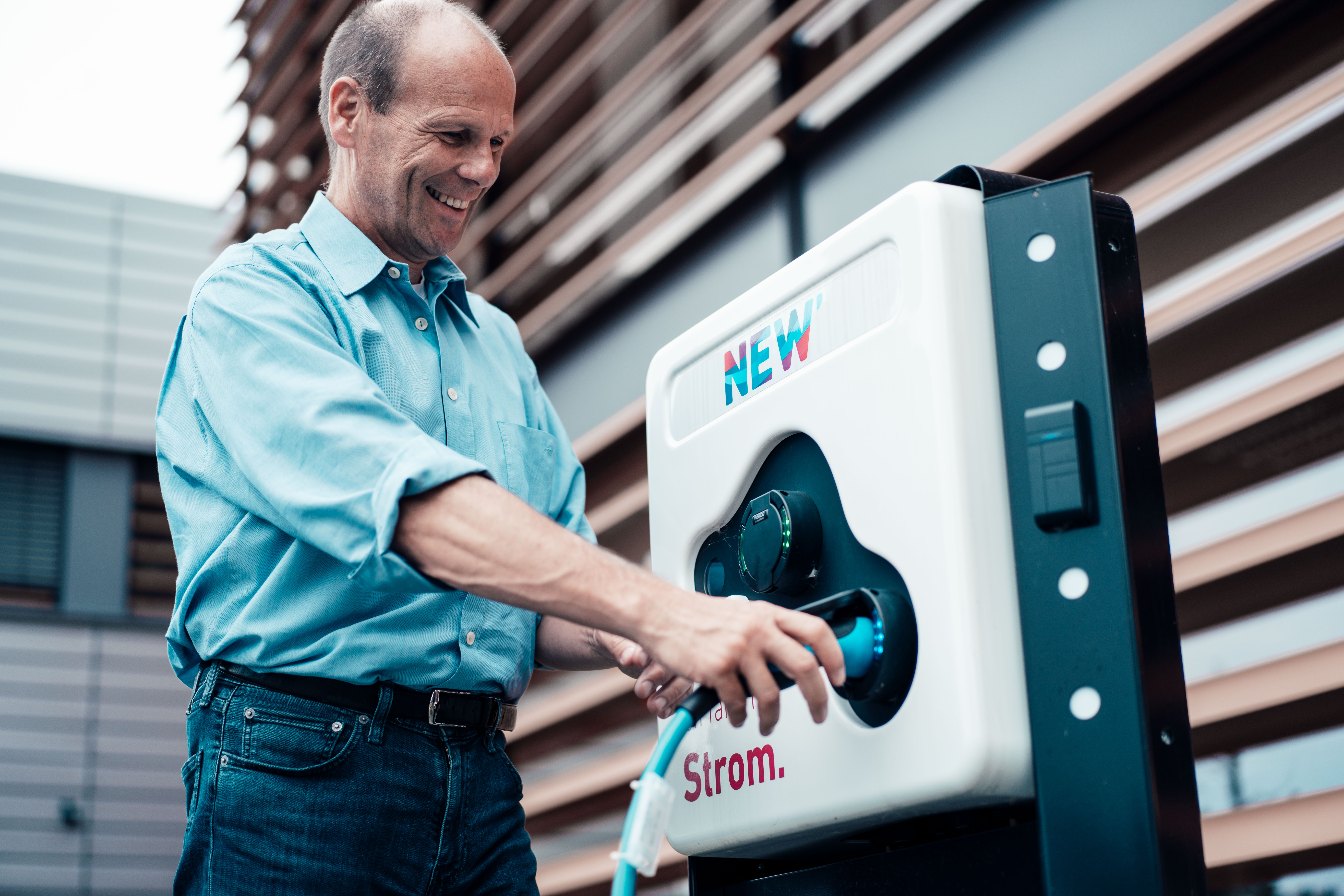 Ein Mann steckt lächelnd ein Ladekabel in eine Ladesäule der NEW Energie