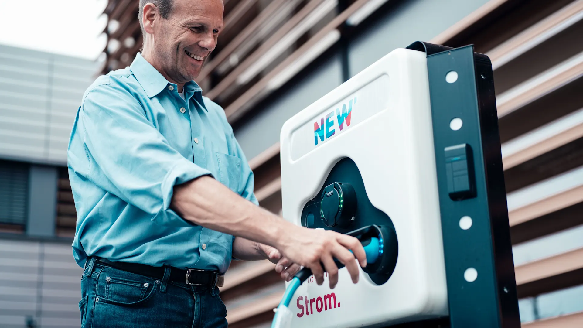 Mann lächelnd an Ladesäule Ein Mann steckt lächelnd ein Ladekabel in eine Ladesäule der NEW Energie
