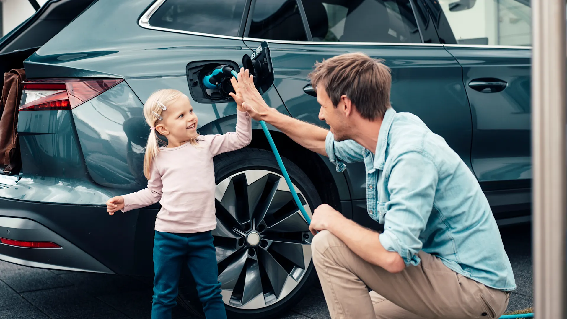 Elektromobilität Vater und Kind haben das Ladekabel an das Elektroauto angeschlossen und laden das Auto mit Autostrom von der NEW Energie.