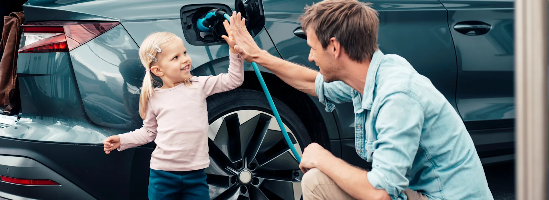 Elektromobilität Vater und Kind haben das Ladekabel an das Elektroauto angeschlossen und laden das Auto mit Autostrom von der NEW Energie.