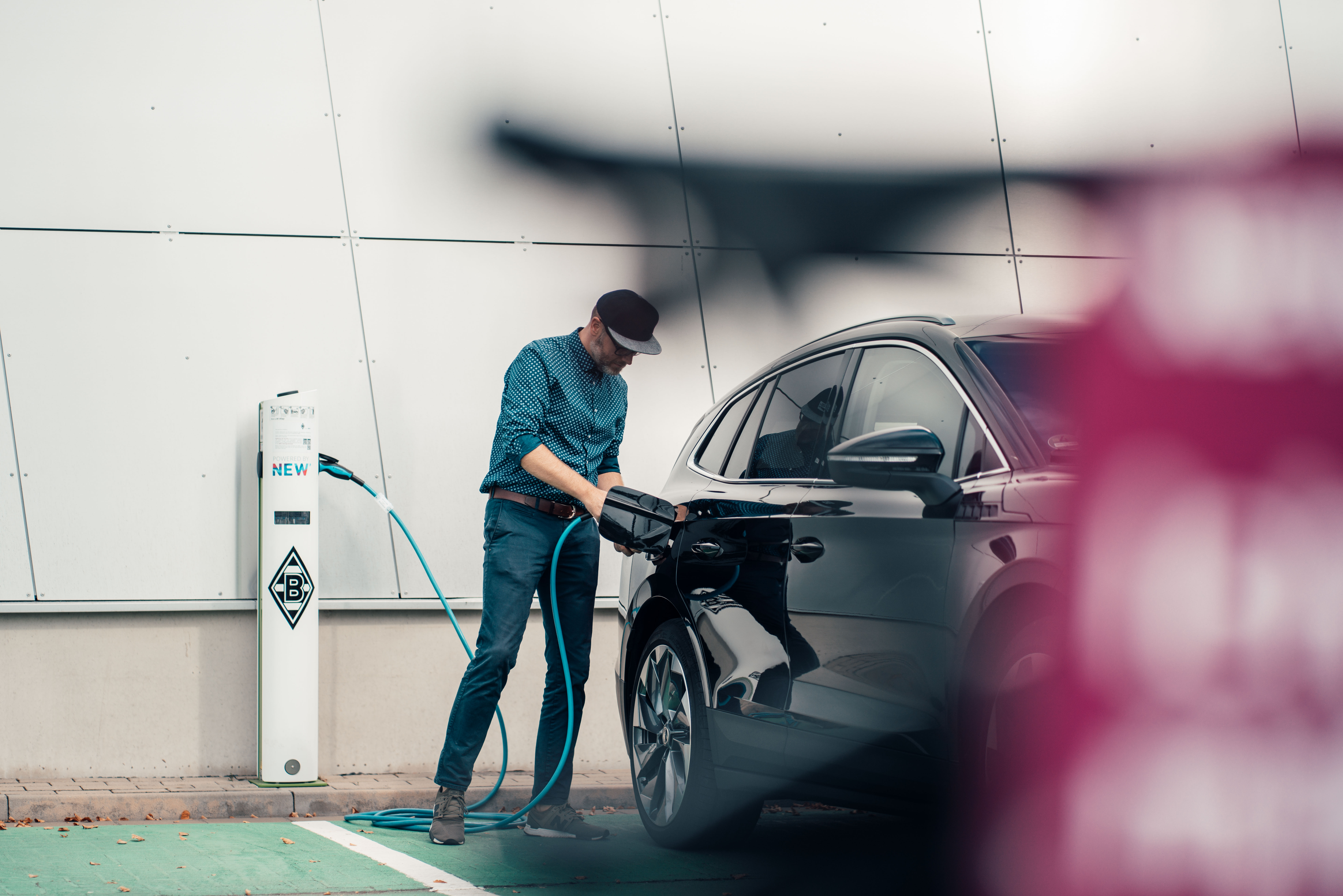 Der Mann lädt auf einem öffentlichen Parkplatz das E-Auto über eine Wallbox auf.