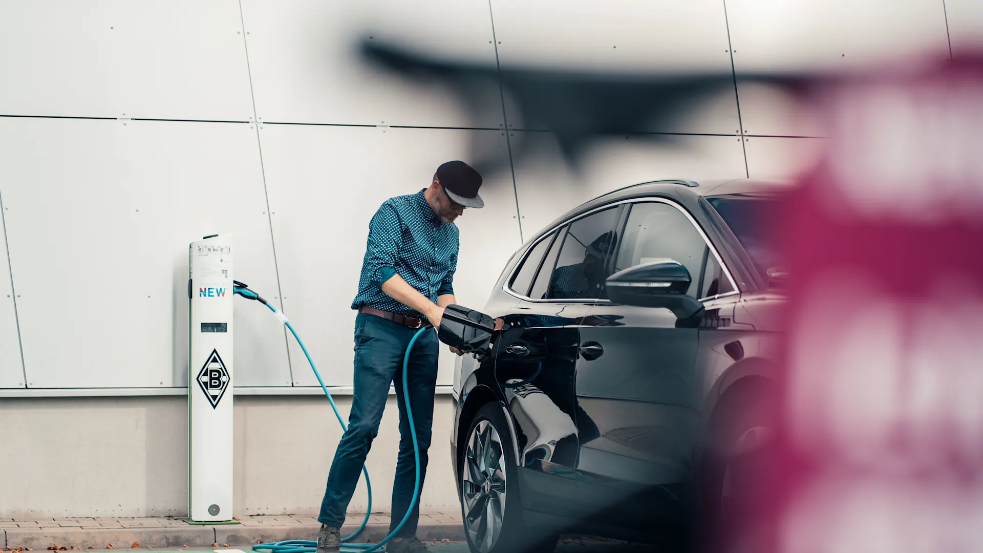 E-Auto wird mit einem Ladekabel an die Wallbox gestellt Der Mann lädt auf einem öffentlichen Parkplatz das E-Auto über eine Wallbox auf.