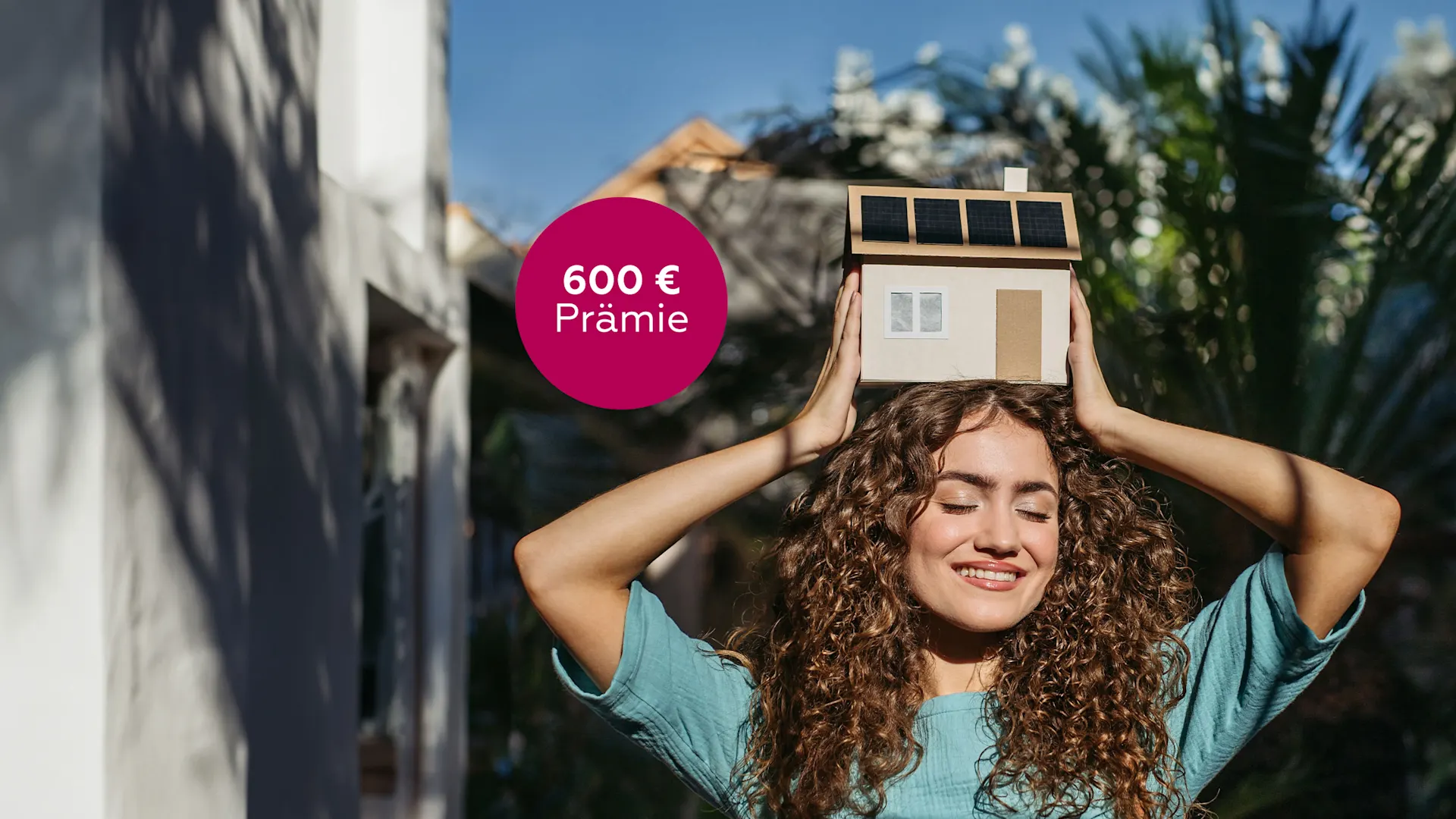 Frau mit PV-Hausmodell über dem Kopf Frau hält sich draußen ein kleines Haus-Modell mit Solarpaneelen auf dem Dach über den Kopf.