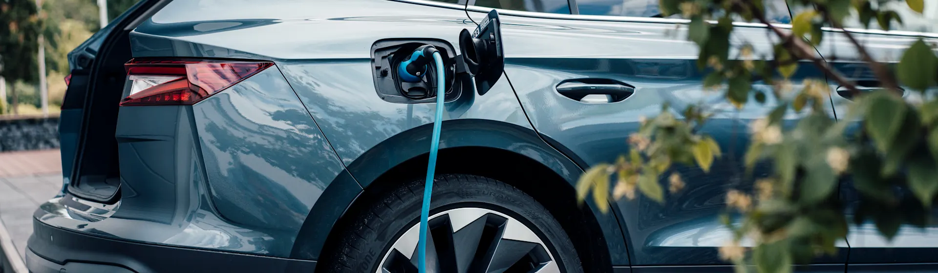 Mit günstigem Autostrom das E-Auto laden Ein Elektroauto mit geöffnetem Kofferraum wird vor einer privaten Garage mit günstigem Autostrom der NEW Energie geladen.