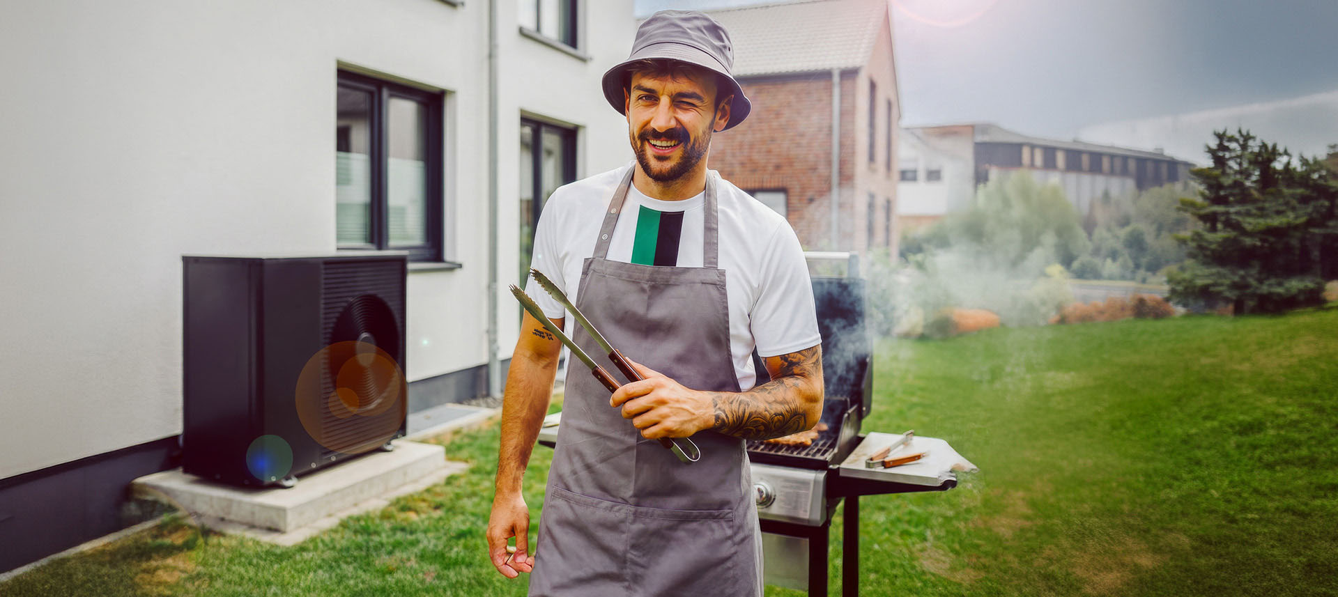 Ein Mann steht vor einem Grill. Links von ihm ist eine Wärmepumpe der NEW Energie zu sehen.