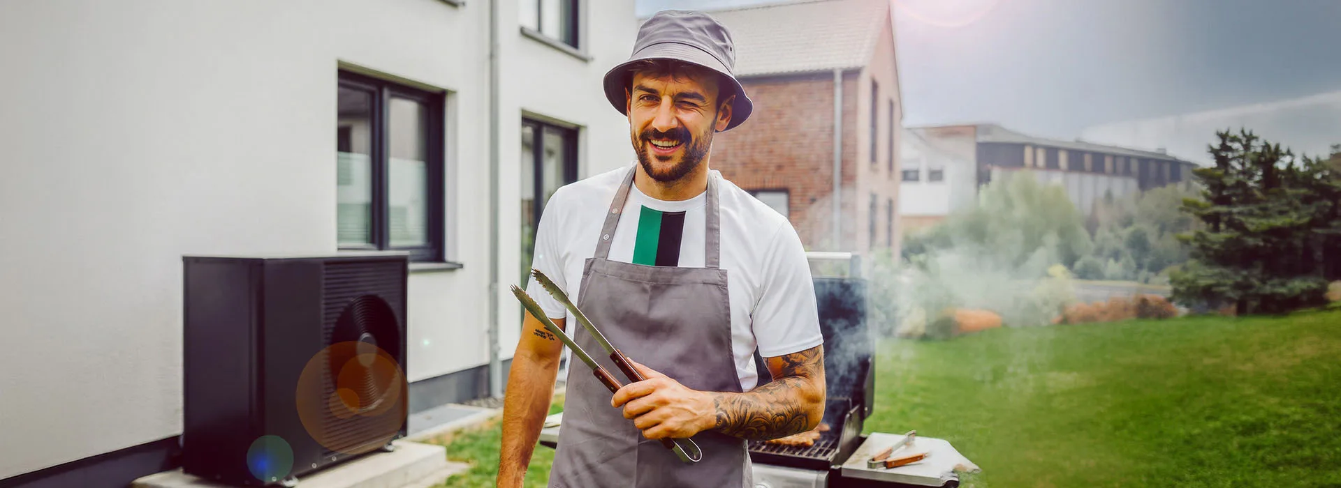 Wärmepumpe bei der NEW Energie Ein Mann steht vor einem Grill. Links von ihm ist eine Wärmepumpe der NEW Energie zu sehen.