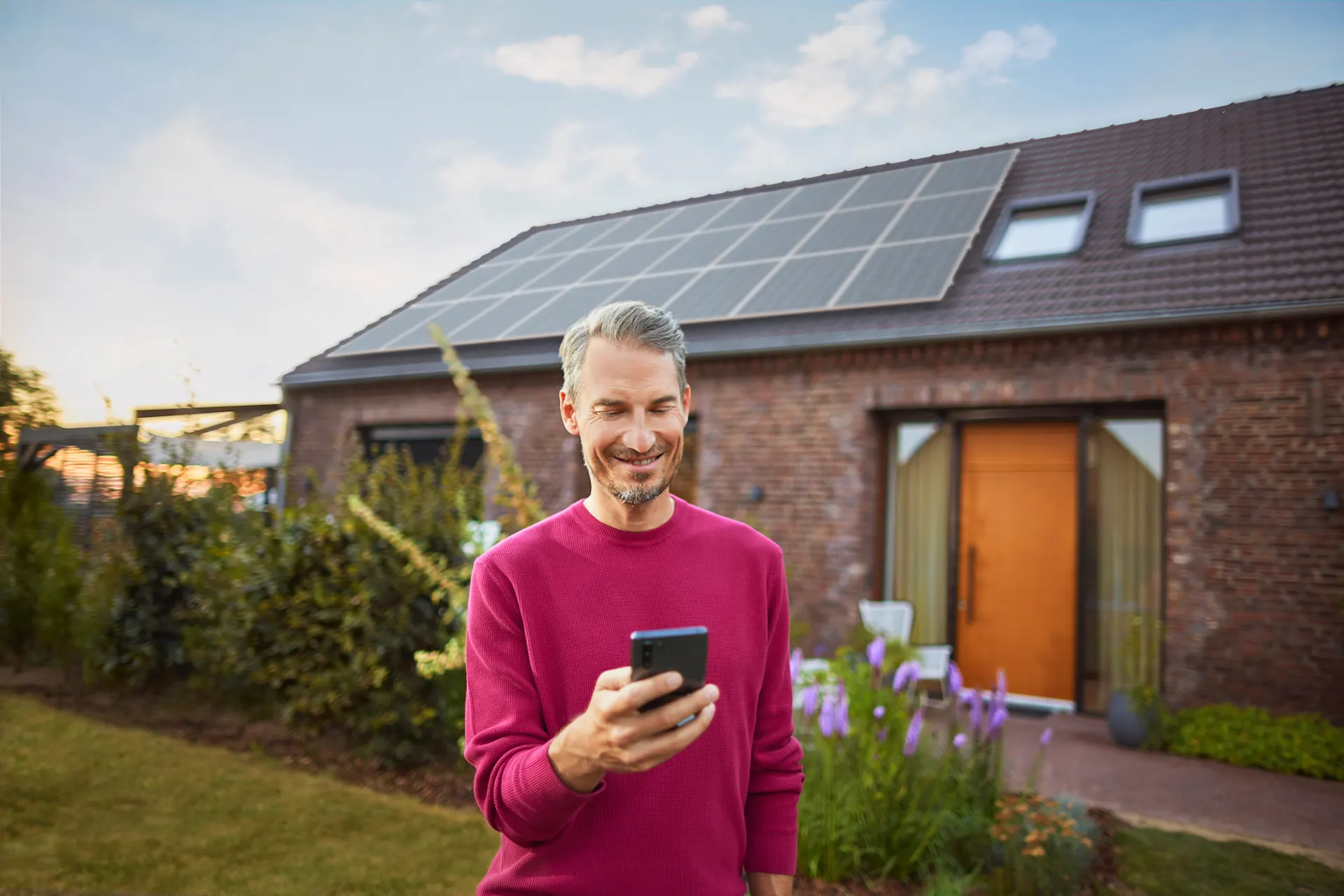 Ein Mann steht mit einem Smartphone im Garten und informiert sich über das Thema Stromerzeugung bei Photovoltaikanlagen bei seinem Energieversorger NEW Energie.