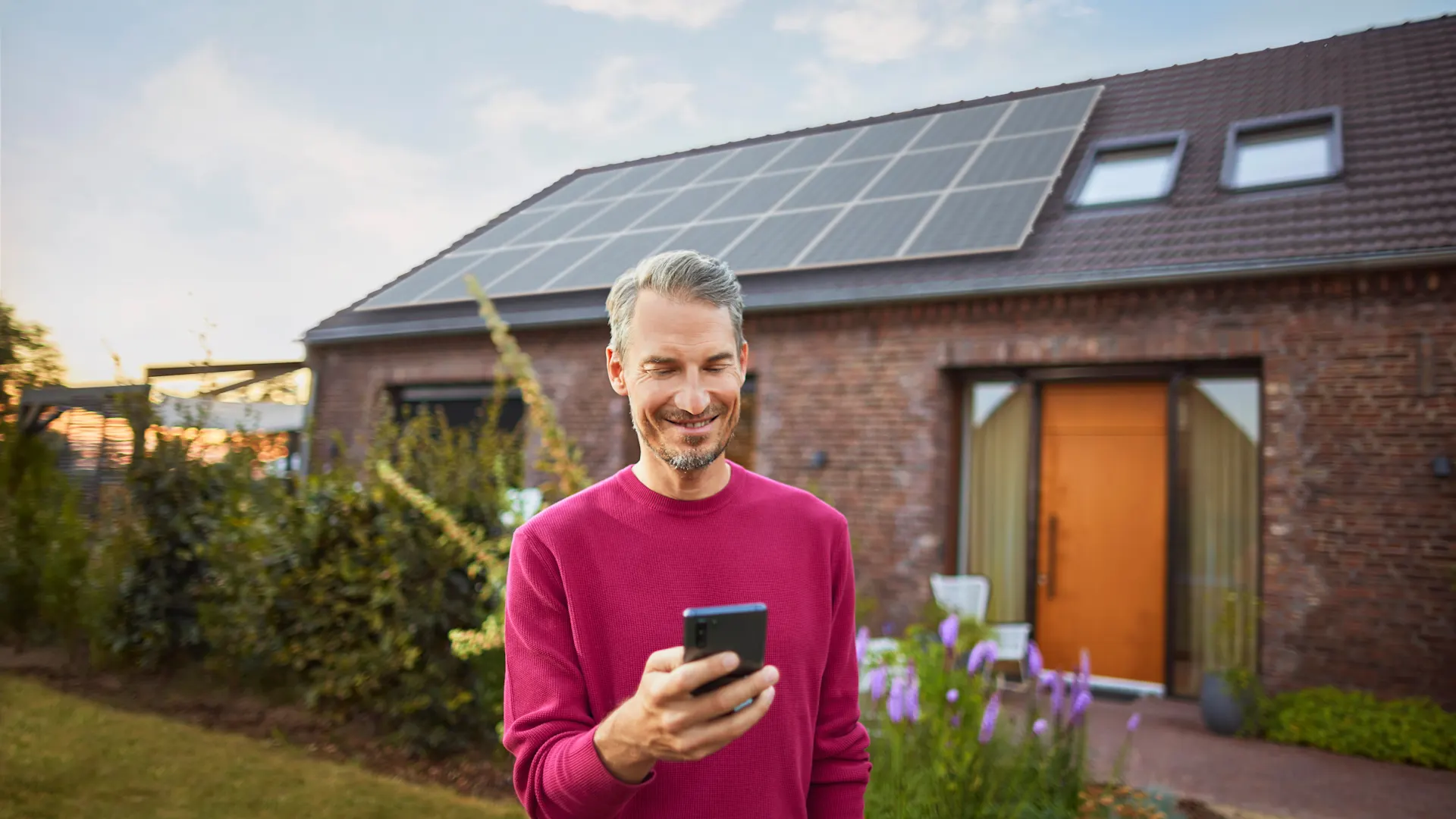 Mann verwendet Smartphone um Angelegenheiten zu klären Ein Mann steht mit einem Smartphone im Garten und informiert sich über das Thema Stromerzeugung bei Photovoltaikanlagen bei seinem Energieversorger NEW Energie.