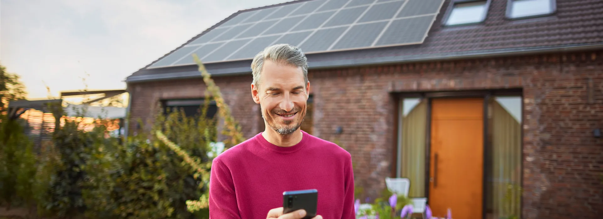 Mann verwendet Smartphone um Angelegenheiten zu klären Ein Mann steht mit einem Smartphone im Garten und informiert sich über das Thema Stromerzeugung bei Photovoltaikanlagen bei seinem Energieversorger NEW Energie.
