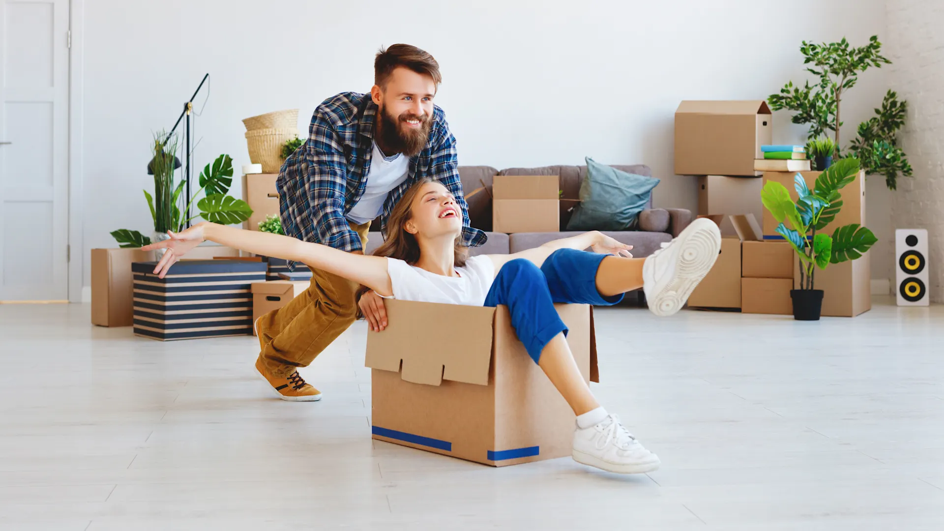 Umzug mit der NEW Energie Ein Paar zieht um. Der Mann schiebt die Frau in einem Karton durch ein Wohnzimmer.