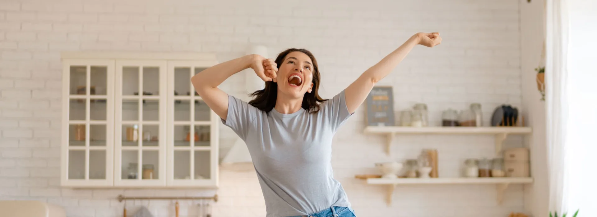 Frau freut sich über günstige Tarife Frau hüpft freudig auf ihrem Sofa, singt und freut sich über günstige Tarife der NEW Energie.