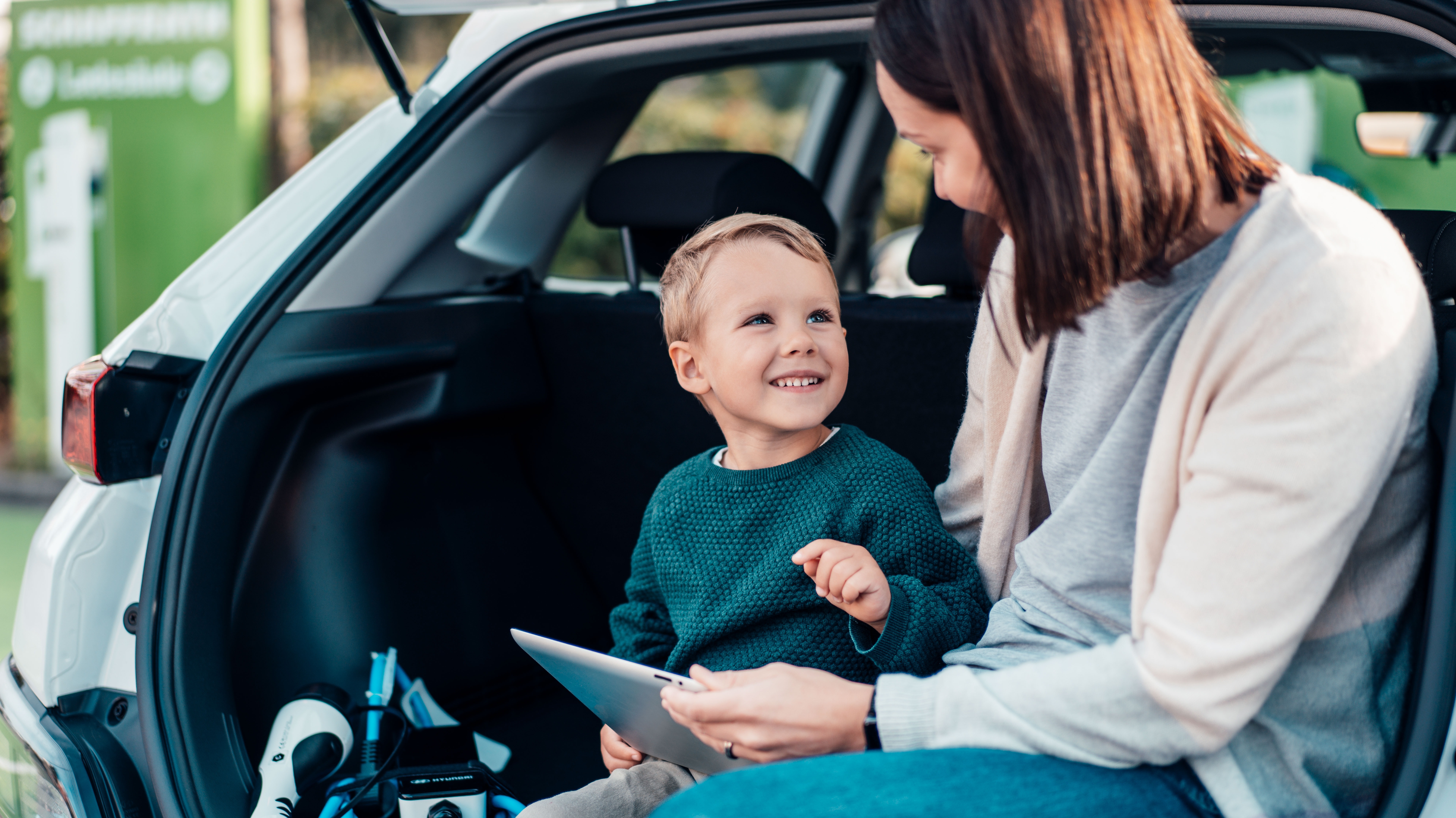 Mutter und Sohn lächeln sich im offenen Kofferraum an und schauen übers Tablet nach Informationen über die NEW Energie.