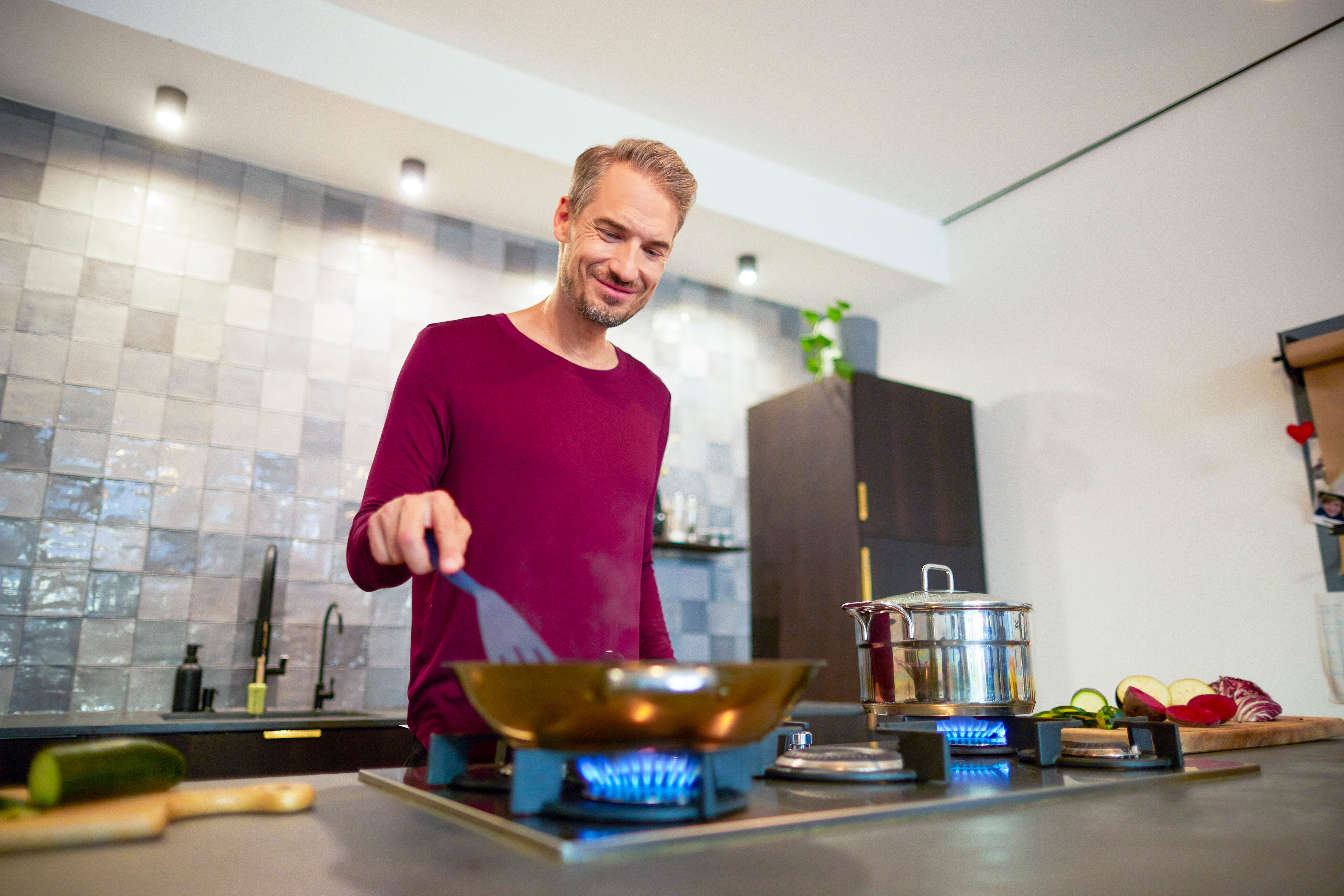 Ein Mann bereitet das Abendessen auf einem Gasherd vor, welcher durch günstiges Ökogas der NEW Energie betrieben wird.