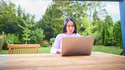 Frau am Laptop bearbeitet Ihren Tarif Eine Frau sitzt mit einem Laptop im Garten und informiert sich über die NEW Energie.