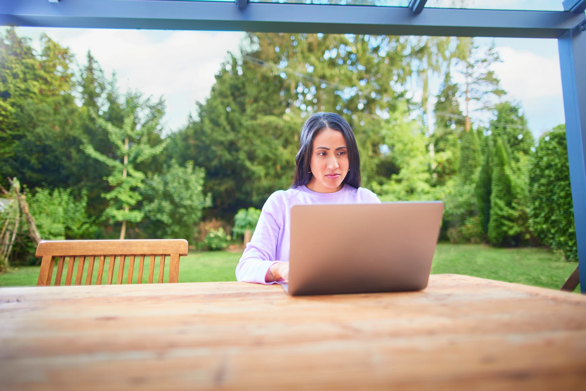 Eine Frau sitzt mit einem Laptop im Garten und informiert.