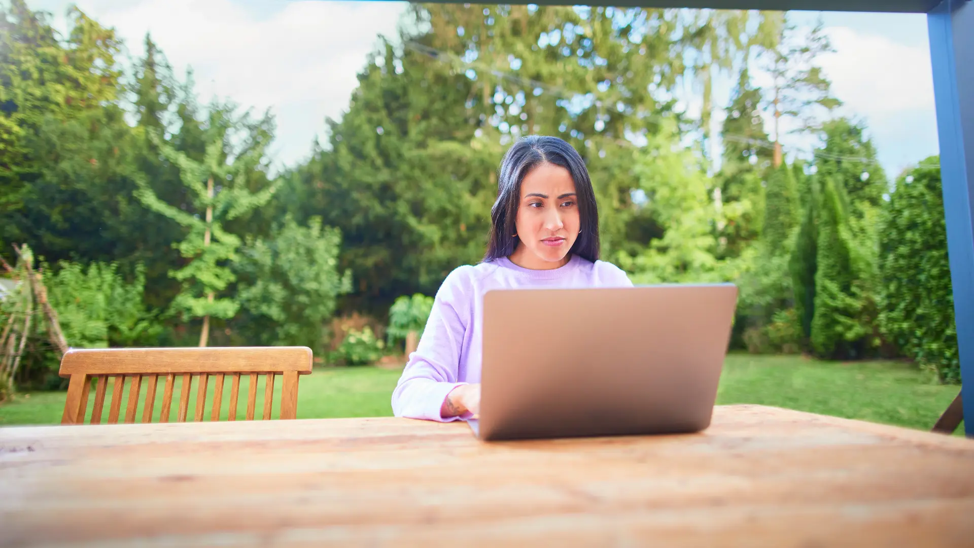 Eine Frau sitzt mit einem Laptop im Garten und informiert sich über den Energieversorger, bearbeitet ihren Tarif und schaut nach Preisanpassungen.