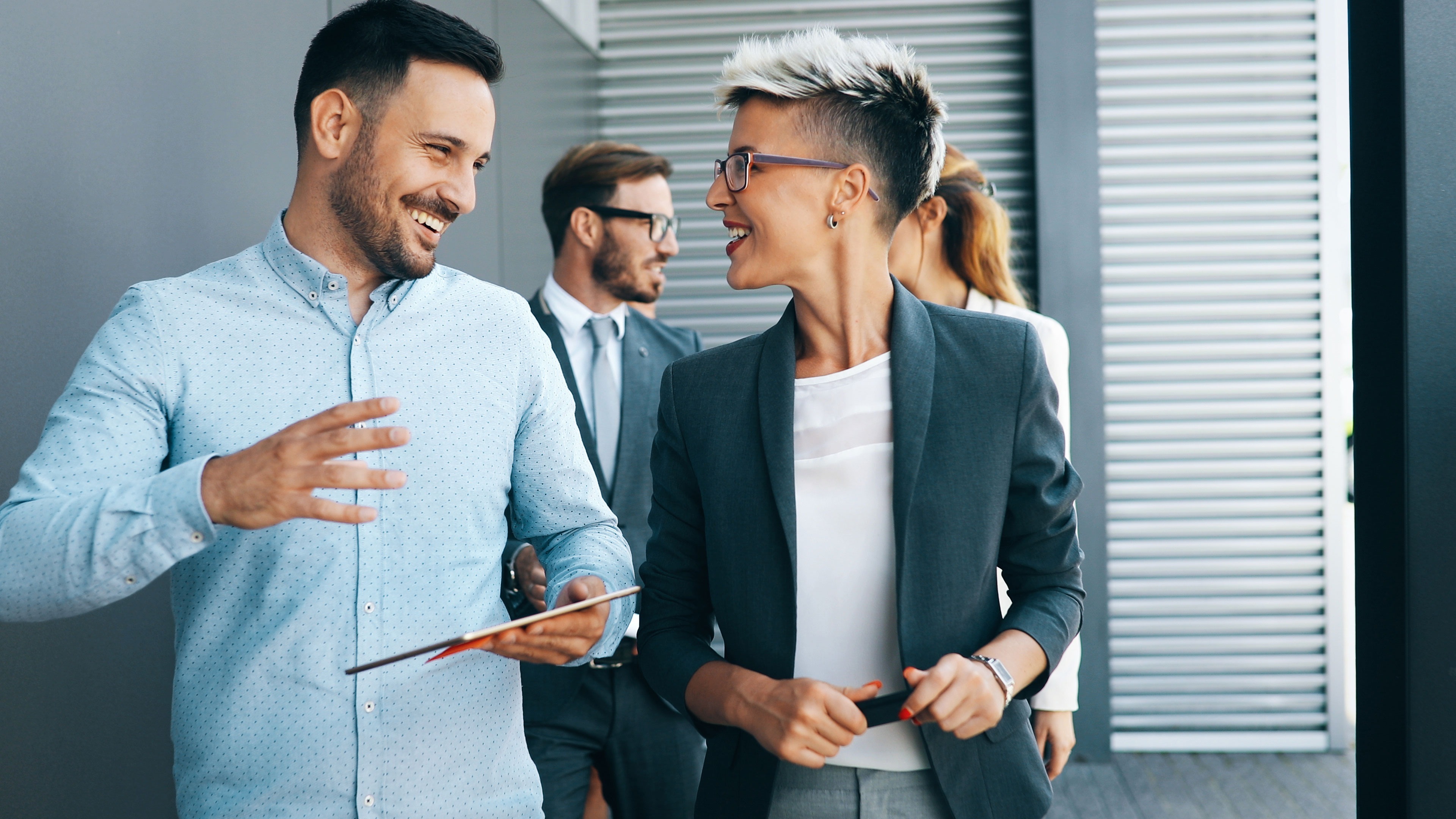 Kollegen sind im Gespräch auf einem Flur und unterhalten sich. Der Mann hält ein Tablet in der Hand.