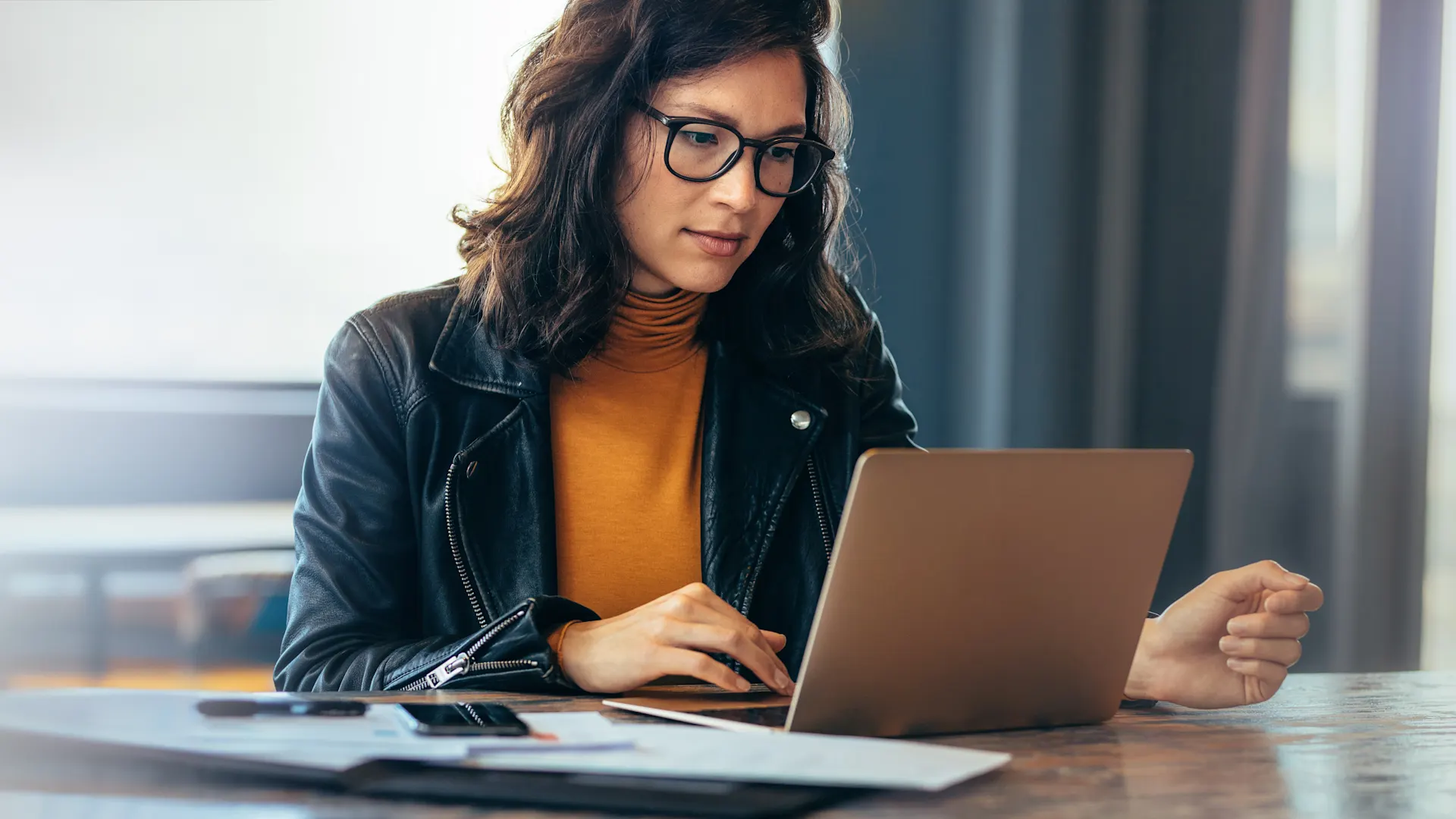 Frau macht sich mit NEW Energie vertraut Eine Frau mit schwarzer Brille sitzt am Tisch vor ihrem Laptop und schaut sich die NEW Energie an.