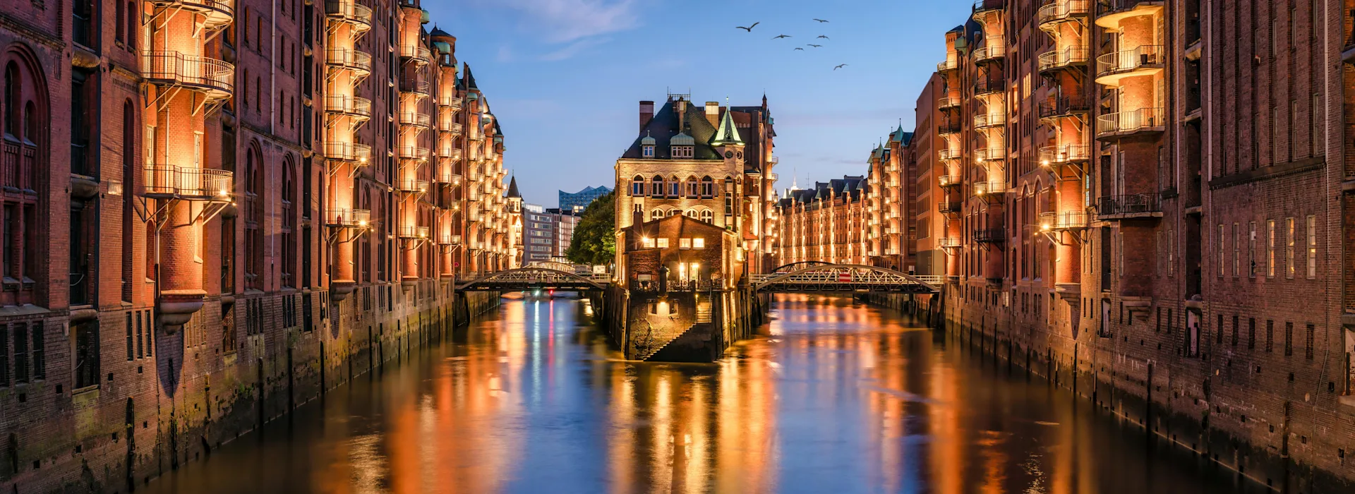 Günstiger Strom für die Hansestadt Hamburg Hamburger Speicherstadt am Abend mit Blick auf das Wasser. Speicherstadt ist beleuchtet. Strom von NEW Energie.