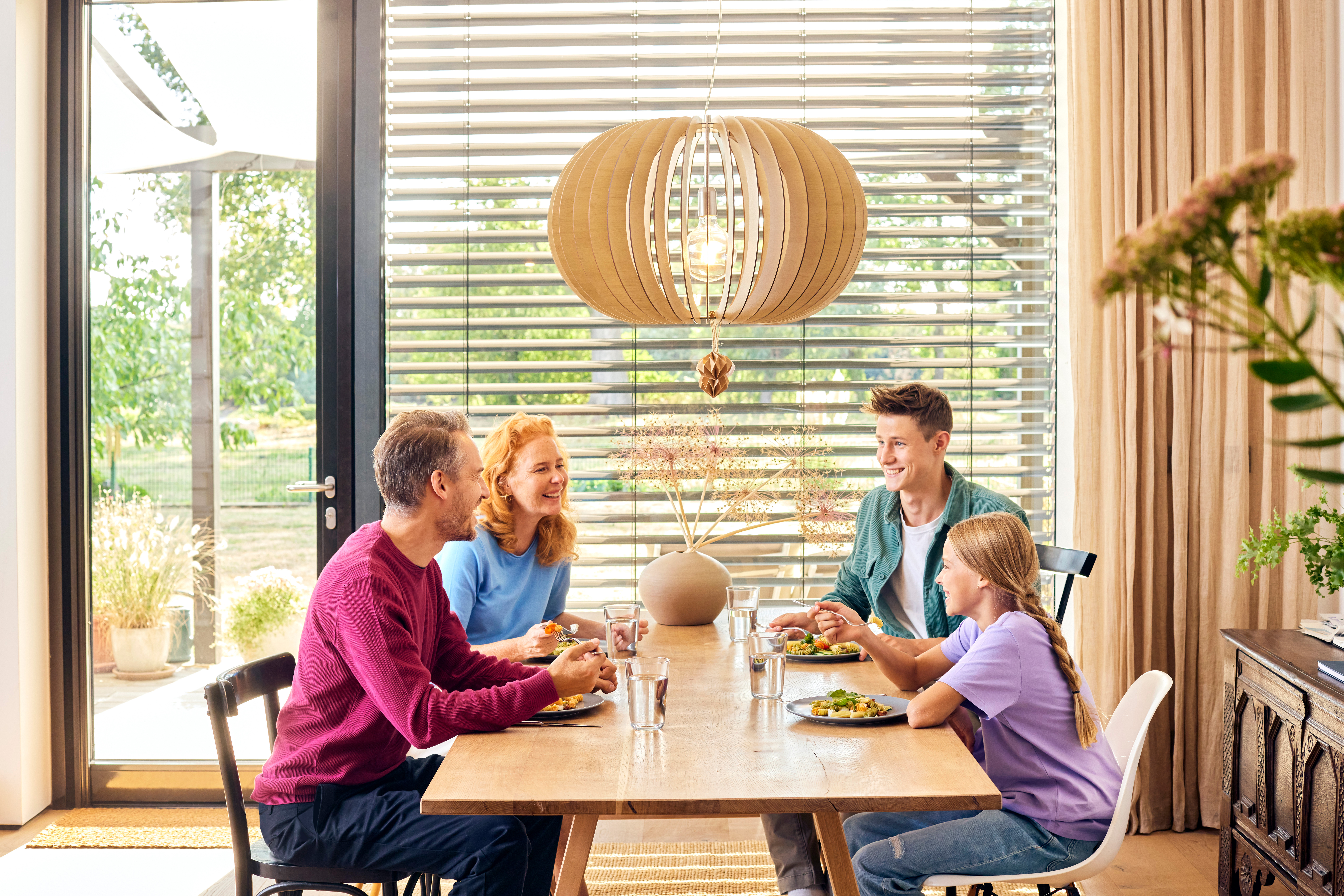 Eine Familie sitzt beim Essen an einem Esstisch und unterhält sich über günstige Tarife bei dem Stromanbieter NEW Energie.