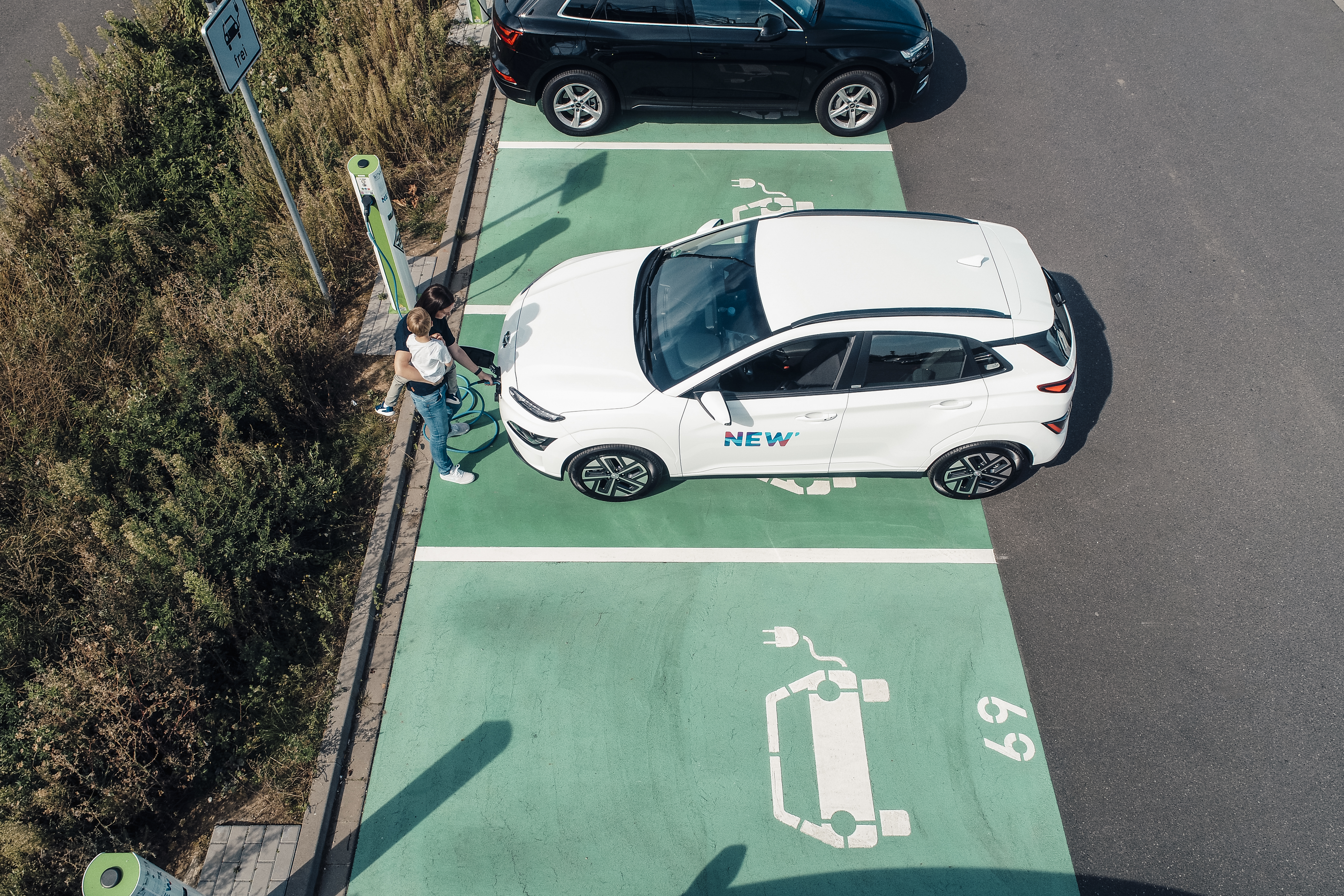 Eine Frau lädt mit einem Kind auf dem Arm das E-Auto auf dem Parkplatz von Borussia Mönchengladbach.