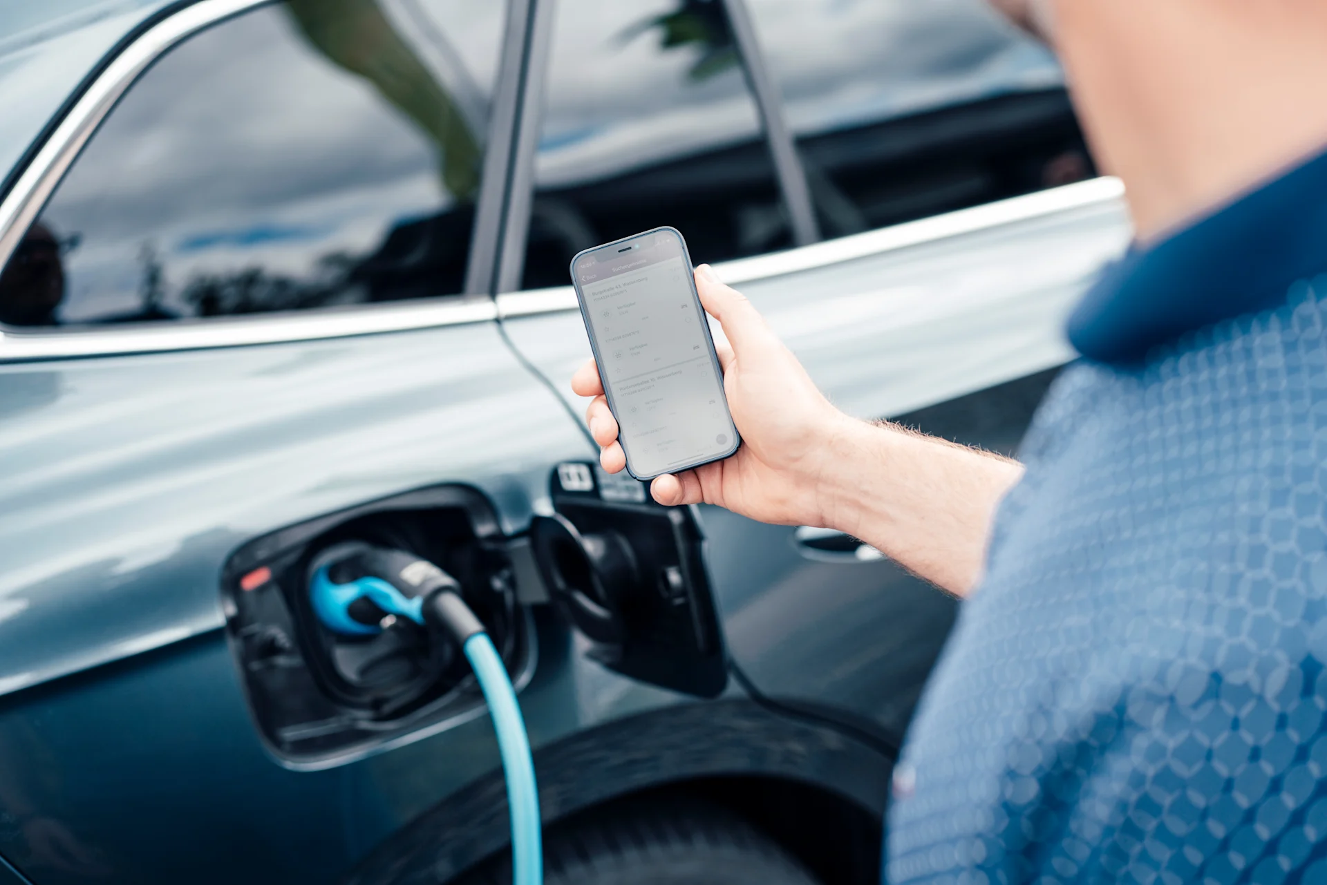 Das E-Auto lädt und der Mann ist auf sein Handy am schauen.