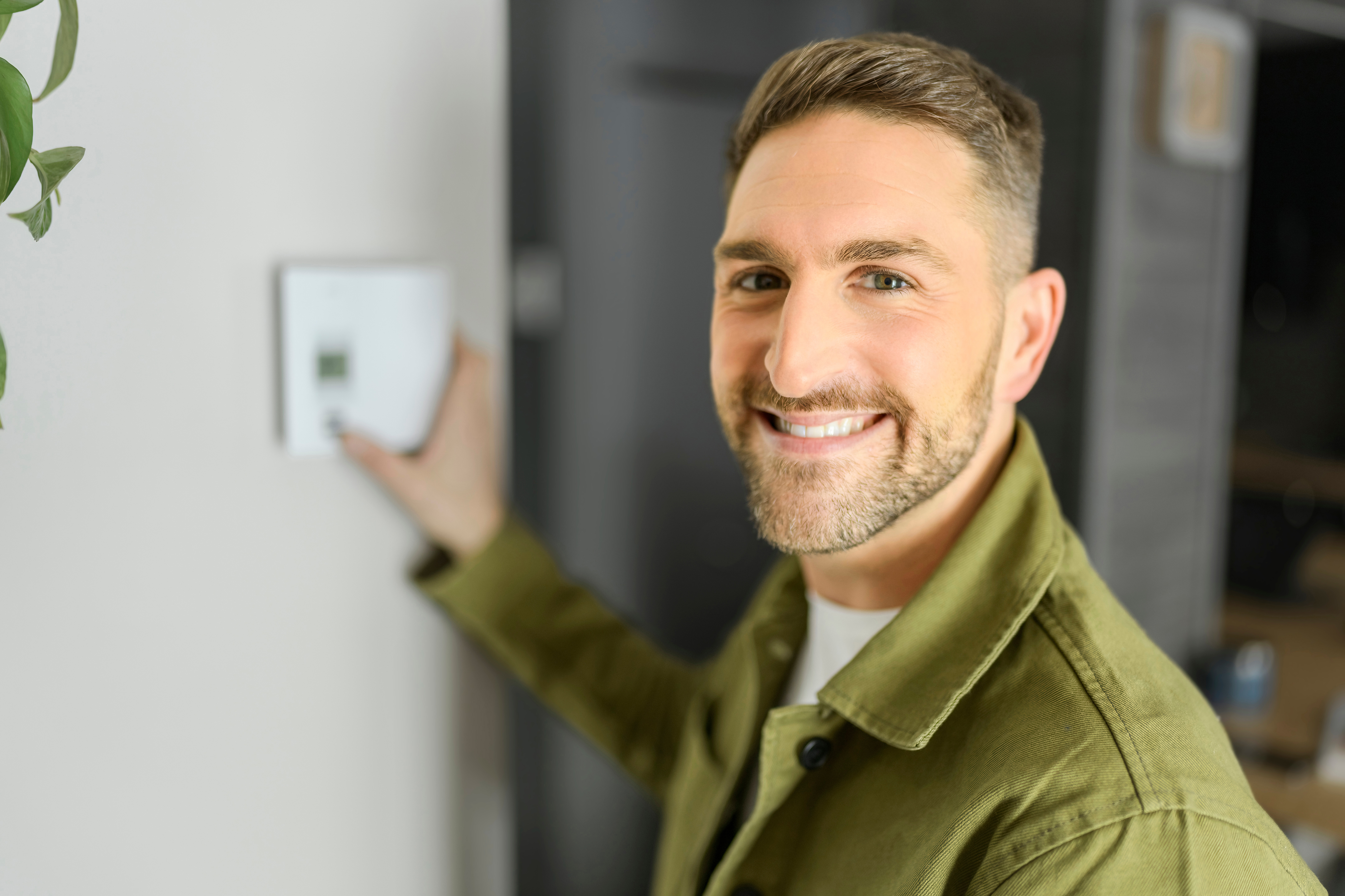 Ein Mann steht lächelnd vor einer Wand, mit der Hand an einem Bedienelement.
