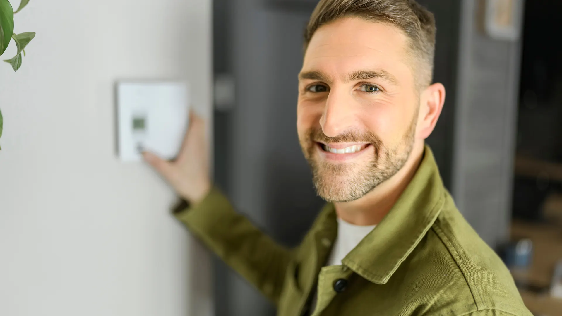 NEWwärme von NEW Energie Ein Mann steht lächelnd vor einer Wand, mit der Hand an einem Bedienelement.