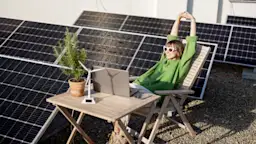 Strom selber erzeugen Die Frau sitzt neben einer Photovoltaikanlage der NEW Energie auf dem Dach.