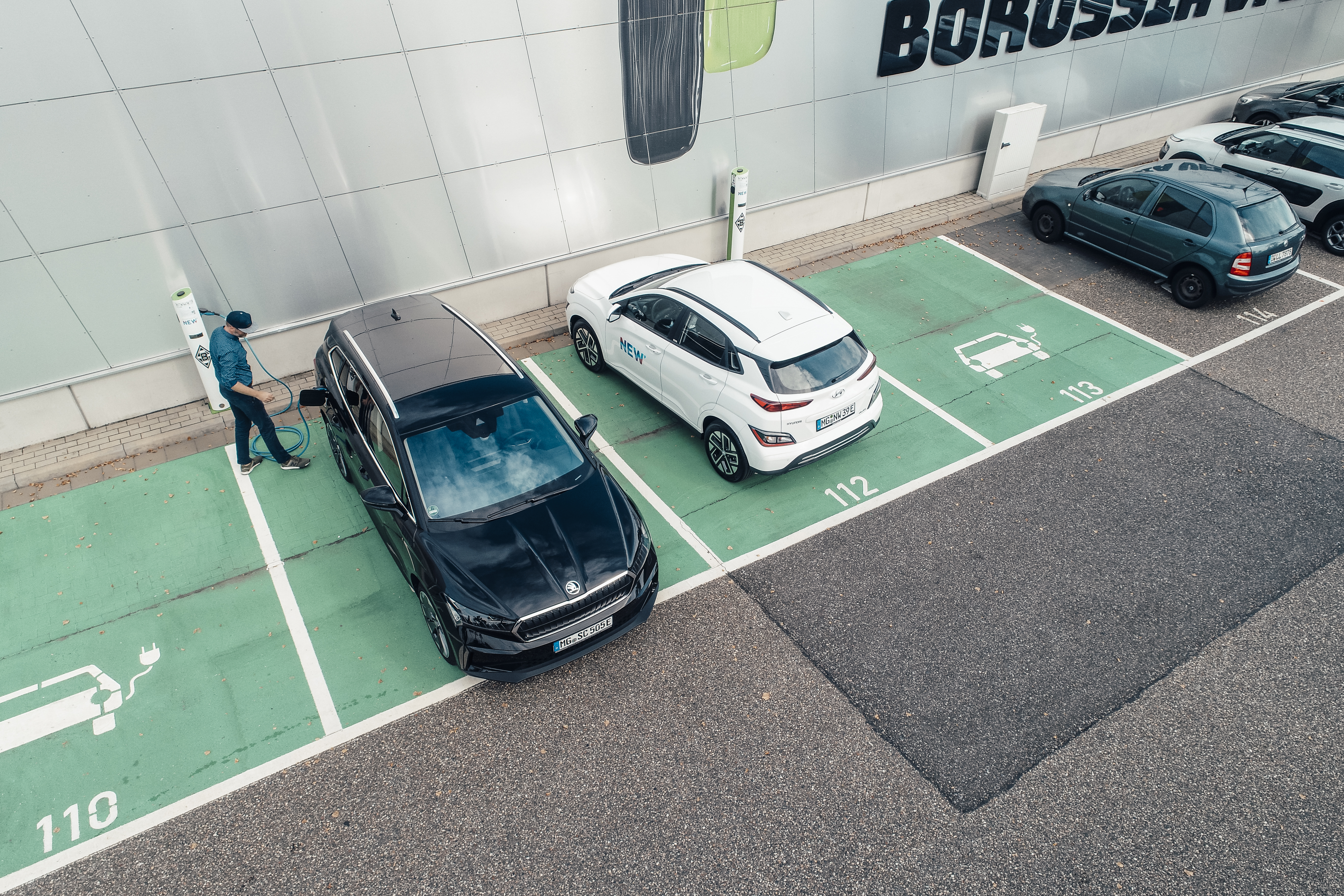 Einige E-Autos stehen auf Parkplätzen zum Aufladen am Borussia-Park. Ein Mann lädt gerade sein Auto an einer NEW-Ladestation auf.