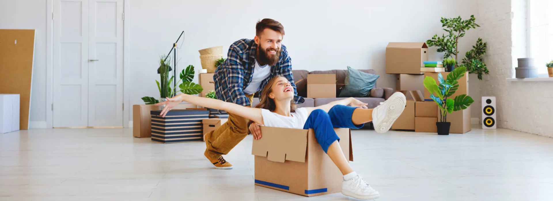 Günstige Energie für Ihr Zuhause Der Mann schiebt in der neuen Wohnung seine Frau mit einem Umzugskarton durch die Wohnung.