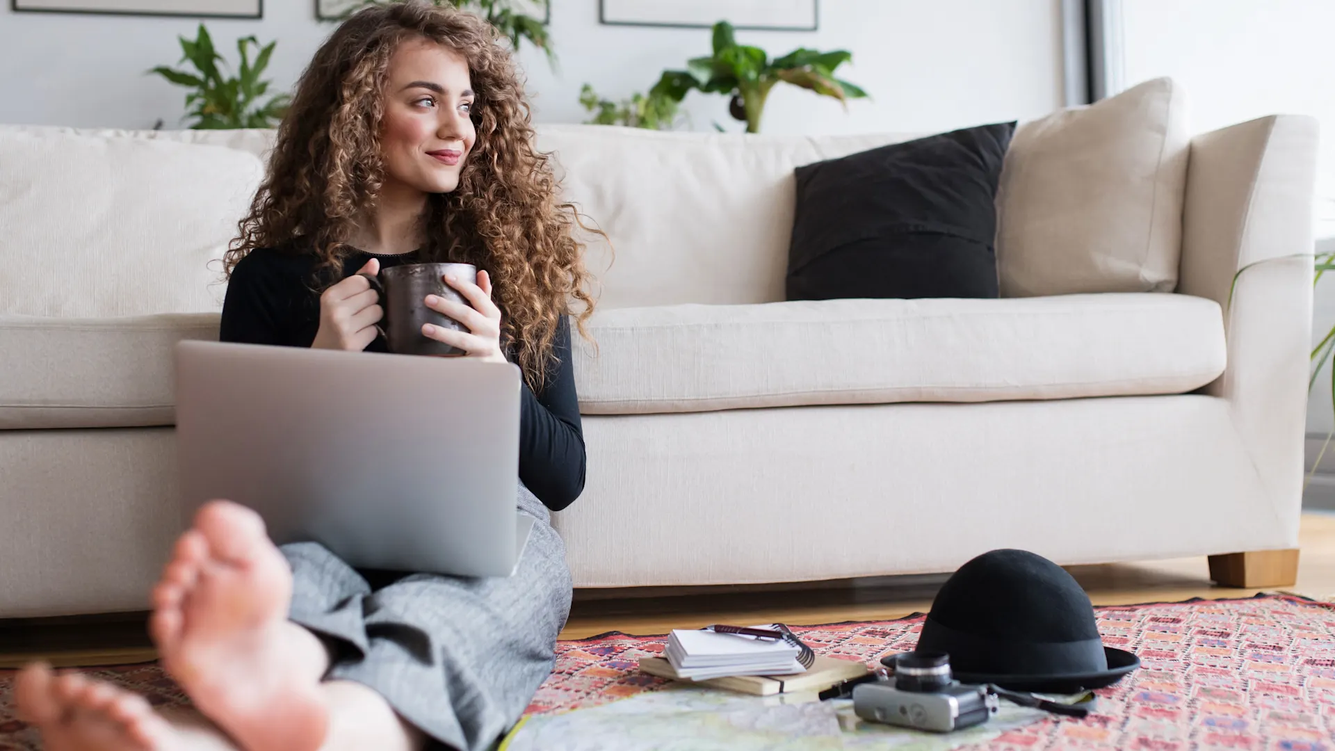 Frau mit Laptop und Kaffee Frau mit Laptop und Kaffee sitzt entspannt vor dem Sofa auf dem Boden und schaut Tarife der NEW-Energie.