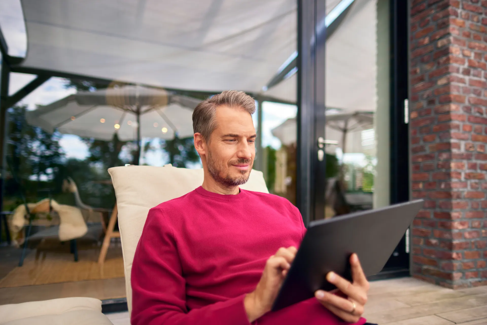 Ein Mann liegt auf einer Gartenliege mit einem Tablet in der Hand und informiert sich über die Produktwelt der NEW Energie, insbesondere über die Stromtarife, Ökostrom und Ökogas.